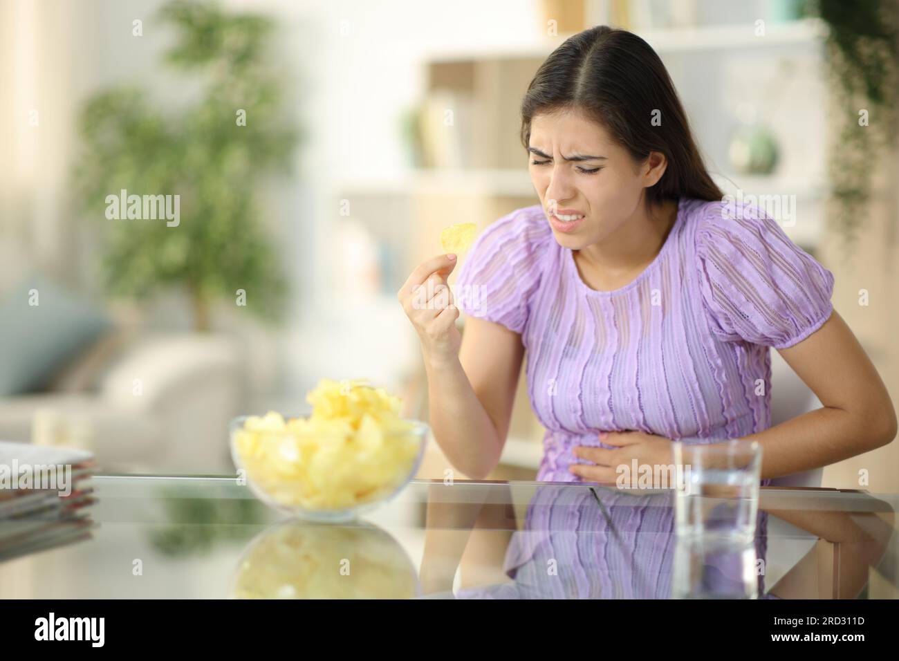 Femme souffrant de maux d'estomac mangeant des chips à la maison Banque D'Images