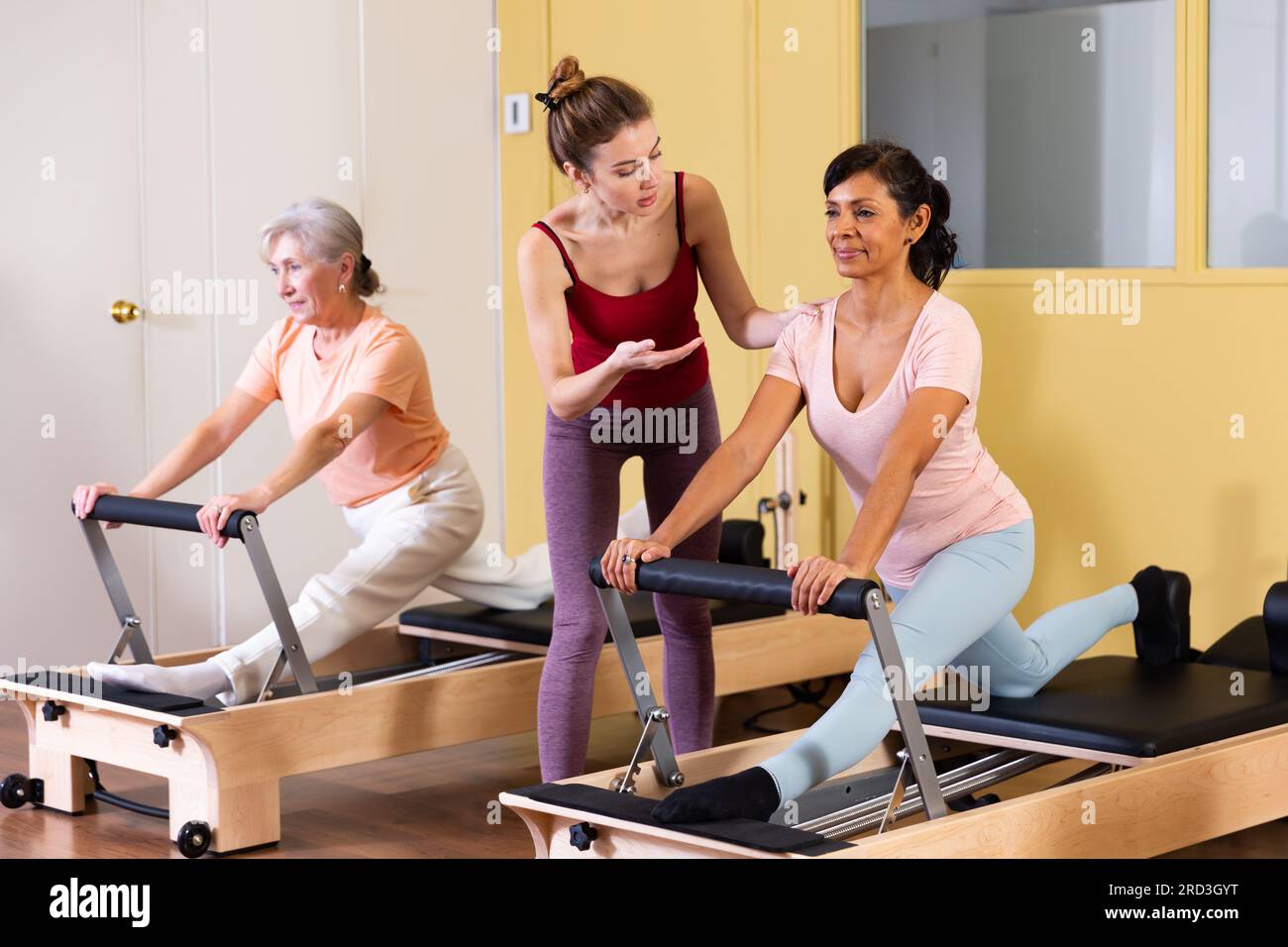 Femme hispanique pratiquant le pilates sur réformateur avec une jeune femme entraîneur Banque D'Images