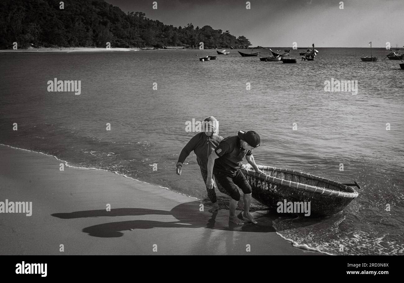 Un mari et une femme vietnamiens reviennent de la pêche et débarquent leur coracle traditionnel à South Beach, son Tra, Danang, Vietnam. Banque D'Images