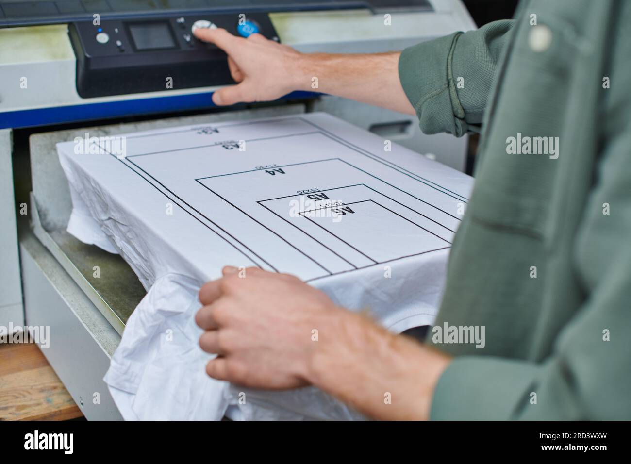 Vue recadrée de jeune artisan flou utilisant la machine de sérigraphie près du t-shirt avec marquage dans le studio d'impression, conce de petite entreprise axée sur le client Banque D'Images