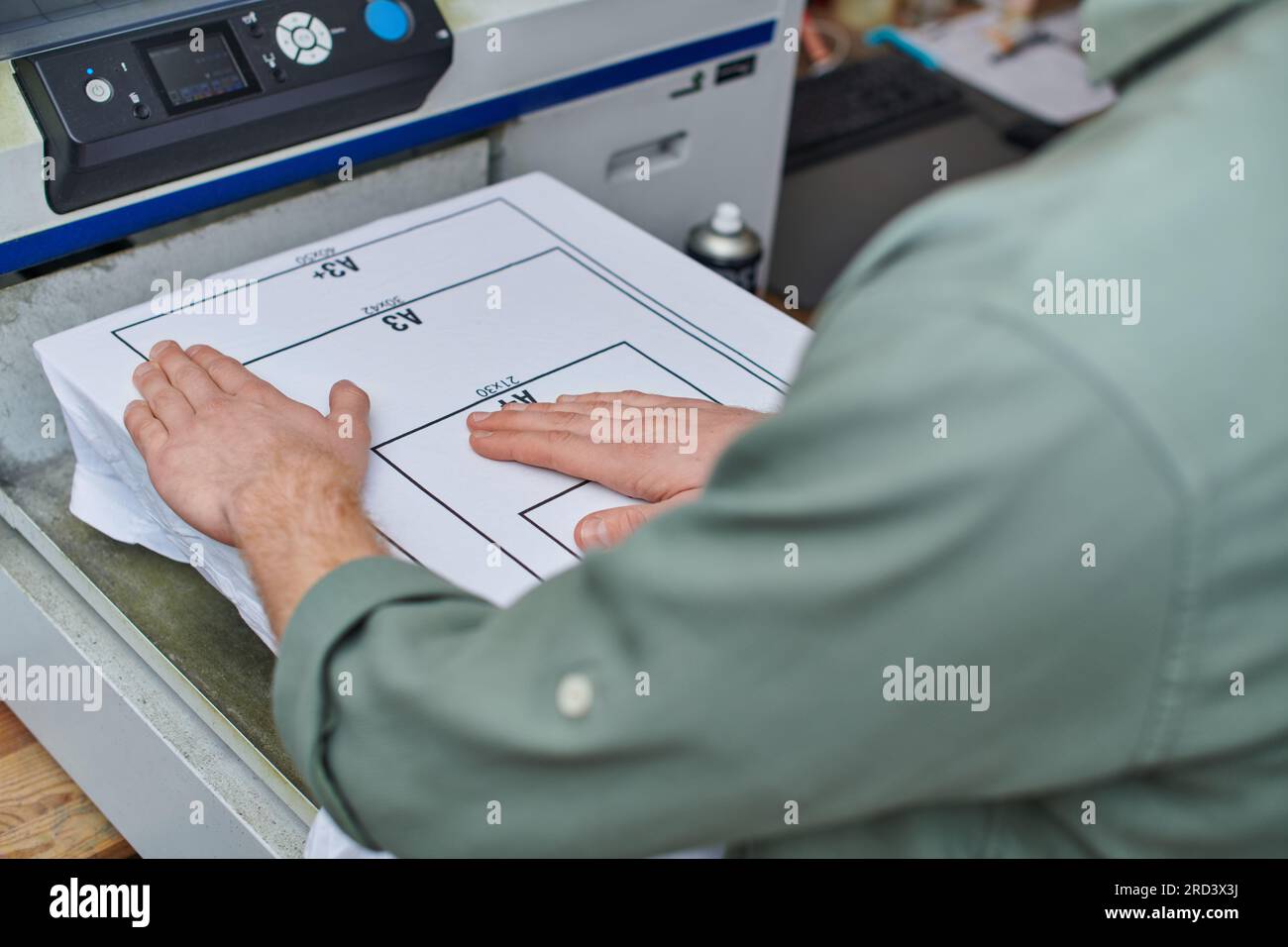 Vue recadrée de jeune artisan travaillant avec un t-shirt avec marquage et machine de sérigraphie dans le studio d'impression, concept de petite entreprise axé sur le client, Banque D'Images