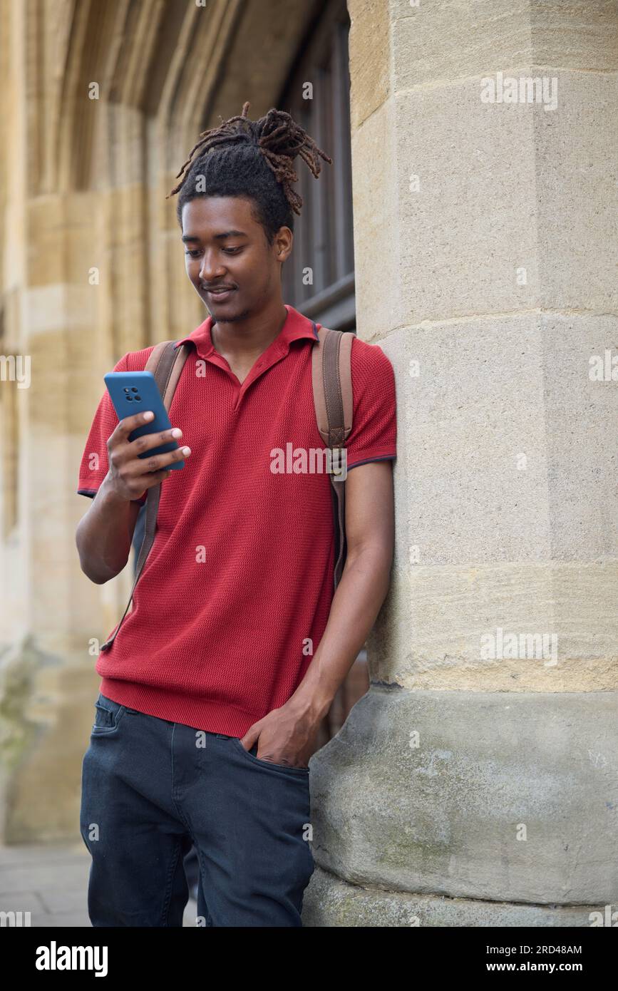 Un étudiant de sexe masculin vérifie les messages ou les médias sociaux sur un téléphone mobile à l'extérieur du bâtiment universitaire d'Oxford, au Royaume-Uni Banque D'Images