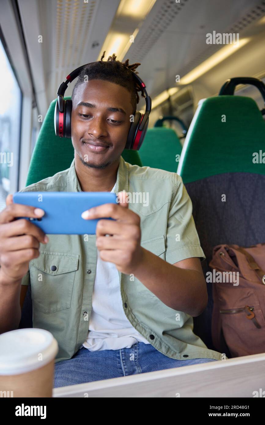 Young Man se rend au travail assis sur le train Streaming et regarder un film ou une émission sur téléphone portable Banque D'Images