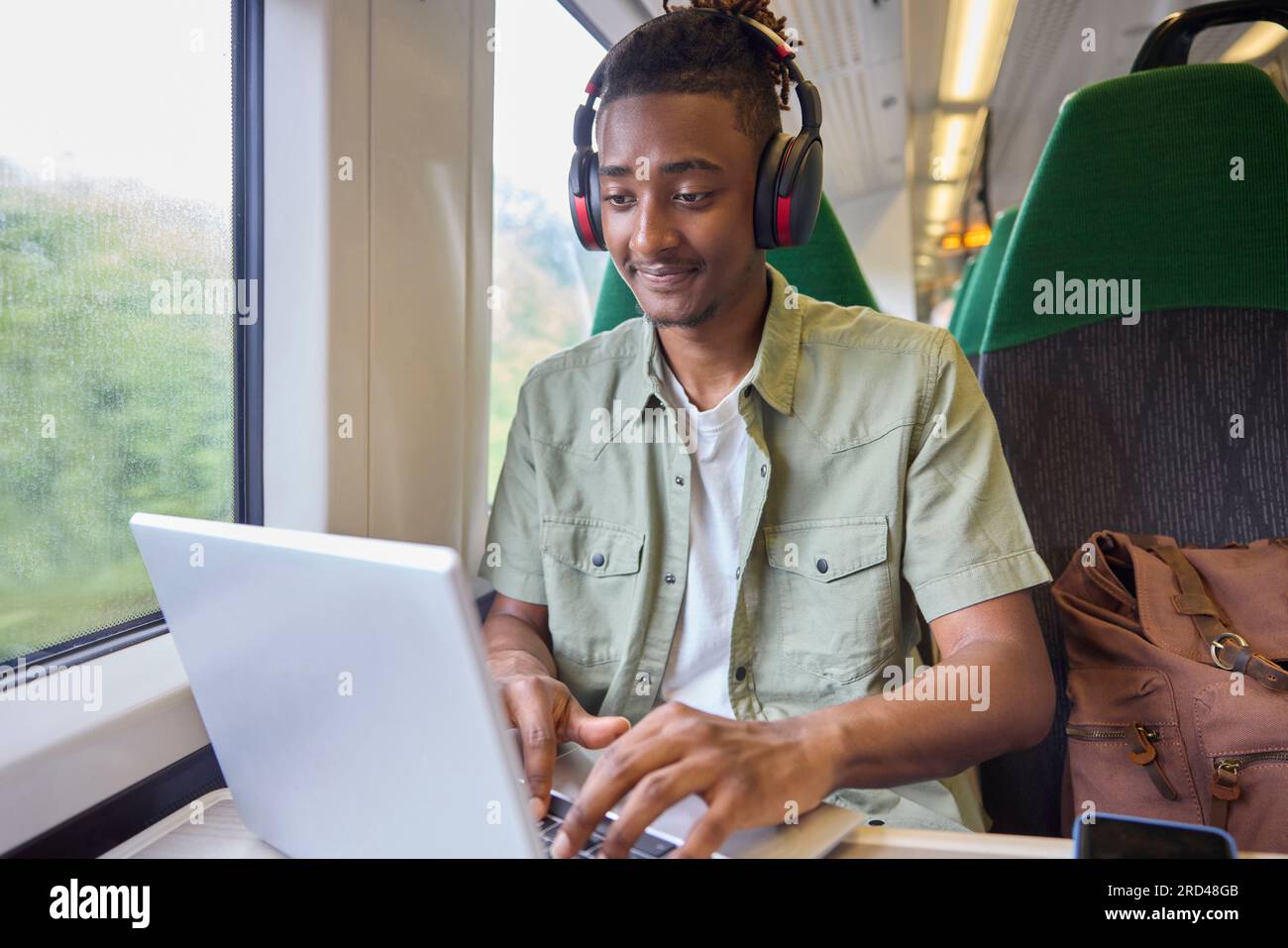 Jeune homme se rendant au travail assis sur le train travaillant sur un ordinateur portable Banque D'Images