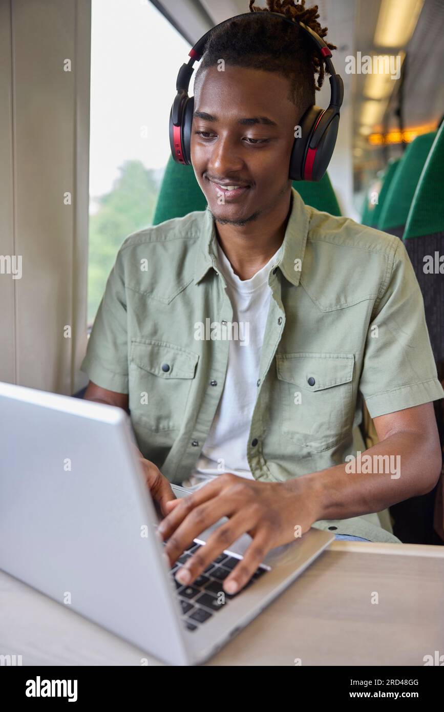 Jeune homme se rendant au travail assis sur le train travaillant sur un ordinateur portable Banque D'Images