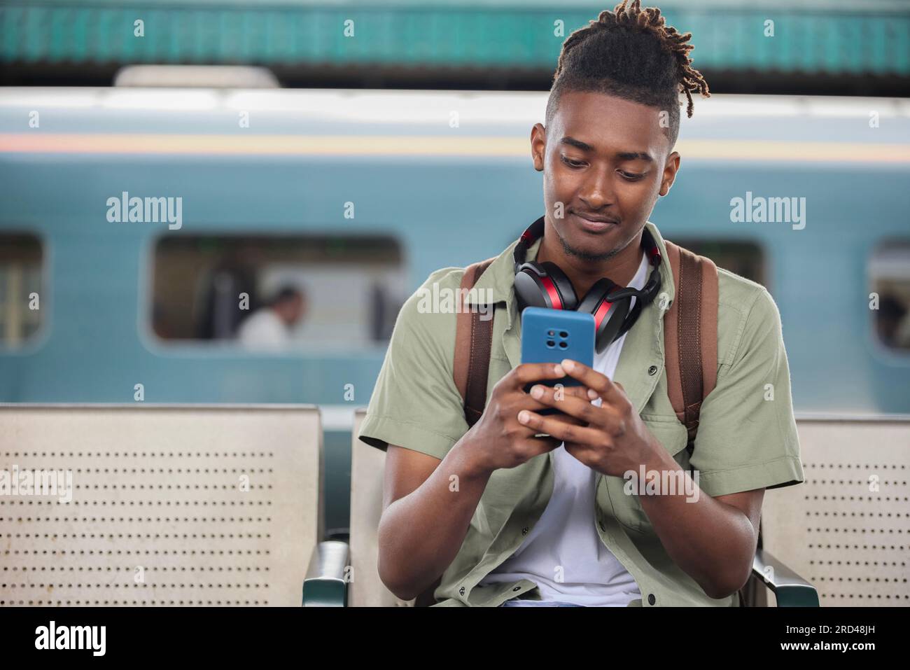 Young Man se déplace pour travailler sur le train assis sur la plate-forme regardant le téléphone portable pour des informations de voyage ou les médias sociaux Banque D'Images