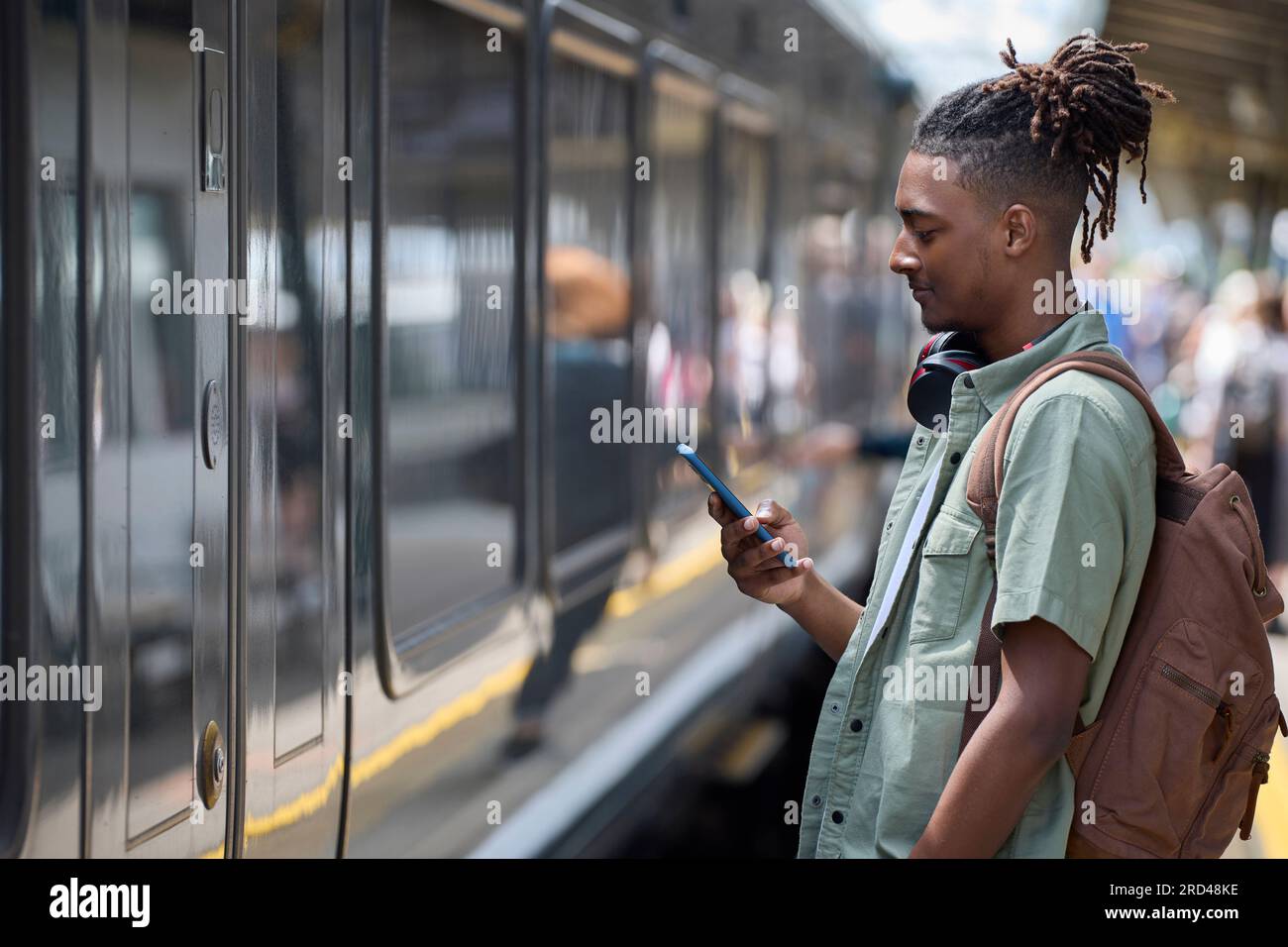 Jeune homme qui se rend au travail sur le train debout sur la plate-forme regardant le téléphone portable à l'arrivée du train Banque D'Images