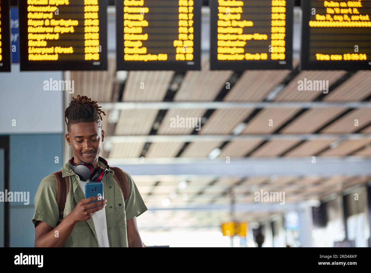 Jeune homme homme portant sac à dos regardant le téléphone portable par train Departure Board dans la gare Banque D'Images