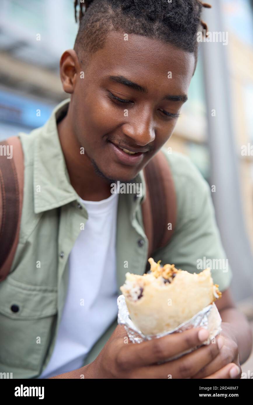 Jeune homme mangeant Burrito à Outdoor Street Food Stall Banque D'Images