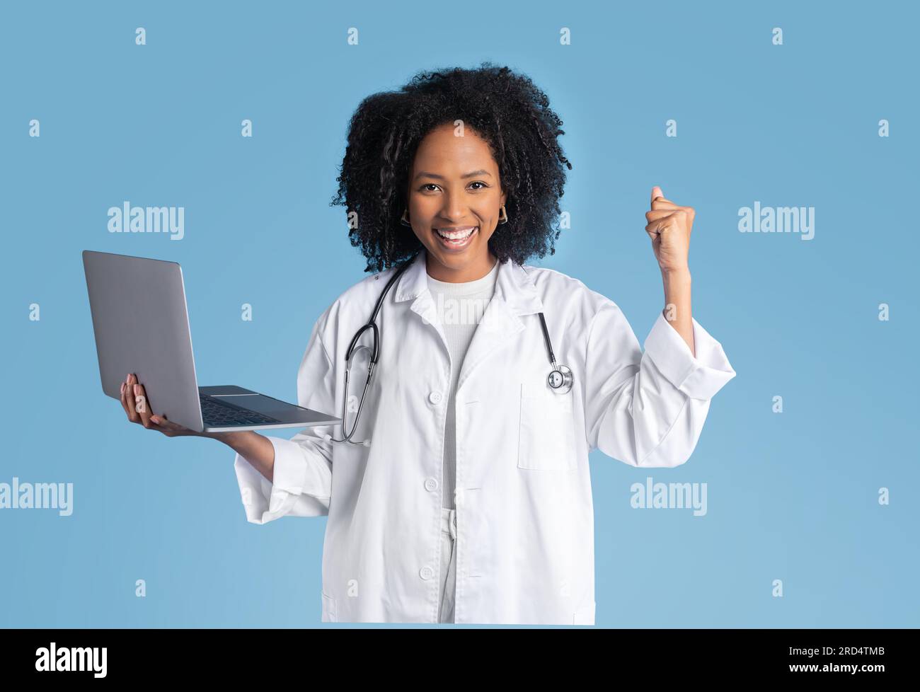 Satisfait jeune femme noire médecin thérapeute en manteau blanc tenir l'ordinateur portable, faisant le geste de main de succès Banque D'Images