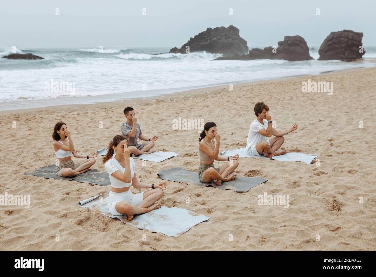Pour guider la respiration. Des jeunes pratiquant le yoga, touchant leur front avec les doigts, assis sur des nattes sur une plage de sable Banque D'Images