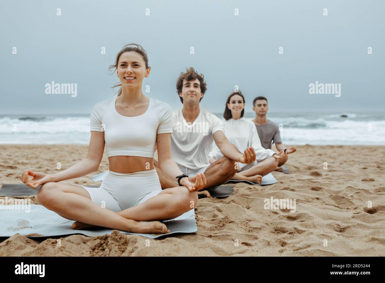 Les femmes et les hommes heureux assis en rangée dans lotus padmasana posent avec pliés dans les mains de signe de mudra, méditant sur la plage Banque D'Images