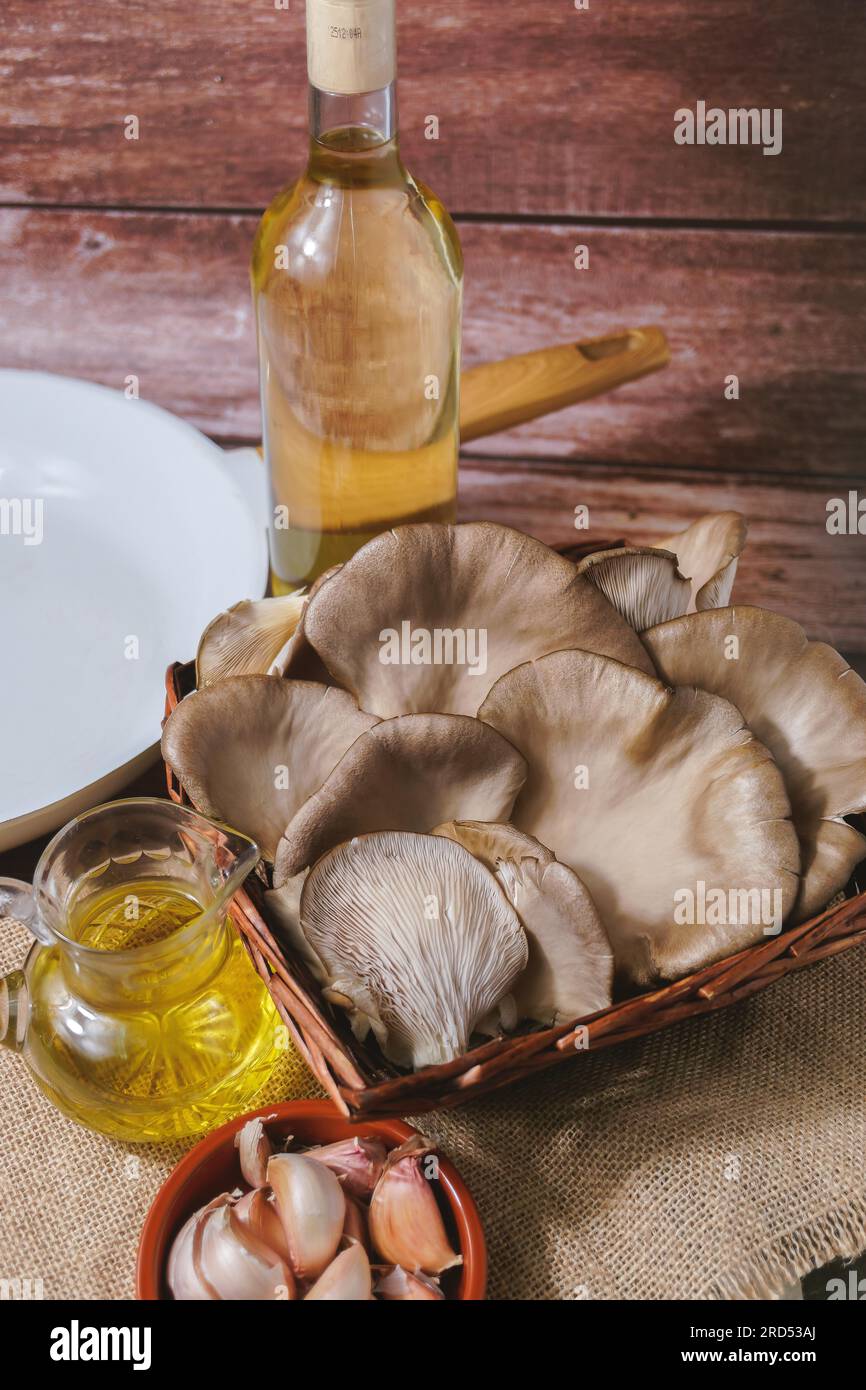 Champignons sauvages ou (Pleurotus eryngii) dans un panier en osier avec des ingrédients pour la cuisson, l'ail et l'huile d'olive Banque D'Images