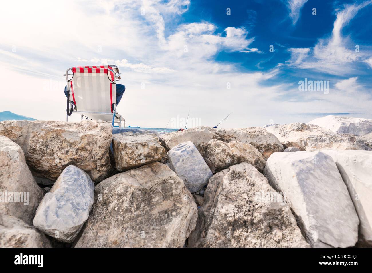 Un homme se repose sur un transat, sur un brise-lames en pierre, contre le ciel bleu, pêchant. Vacances loin de la ville, pêche Banque D'Images