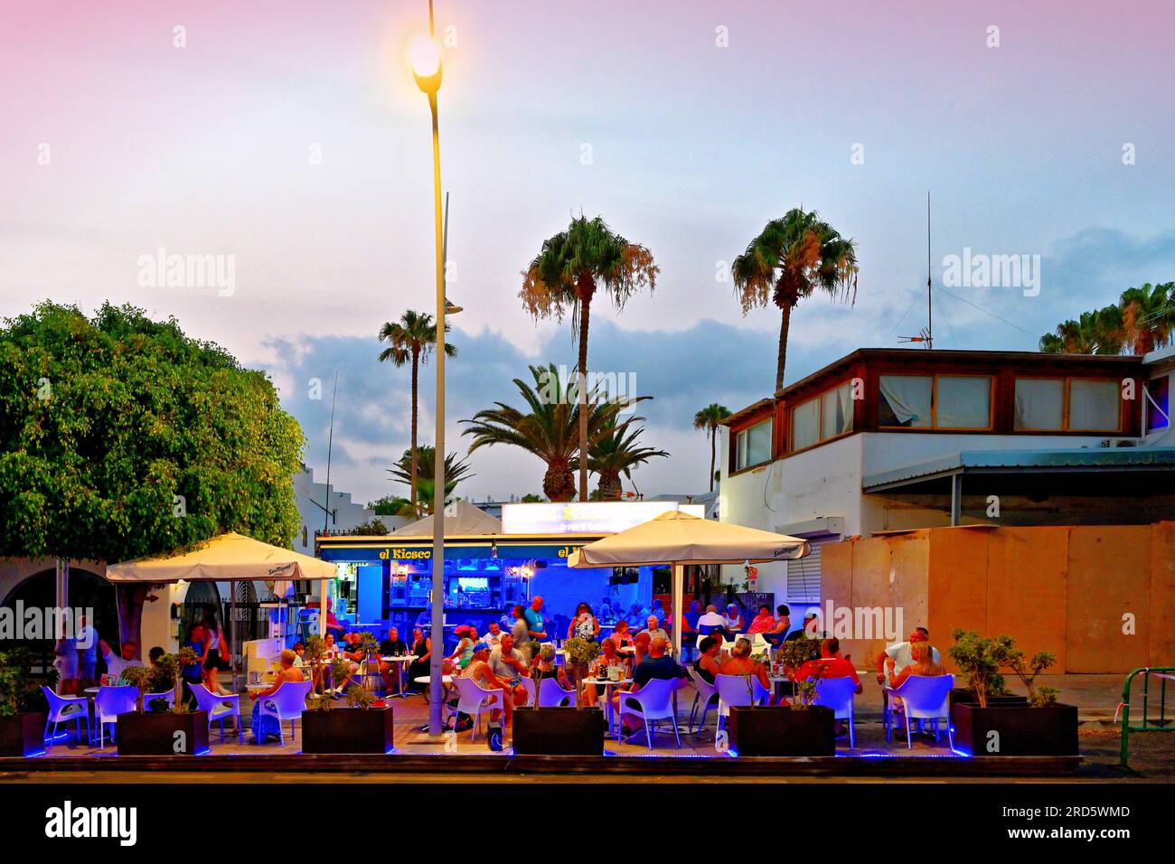 Lanzarote Îles Canaries Puerto Del Carmen El Kiosko pub sur la rue principale et des palmiers avec ciel bleu clair teinté rouge du soir Banque D'Images