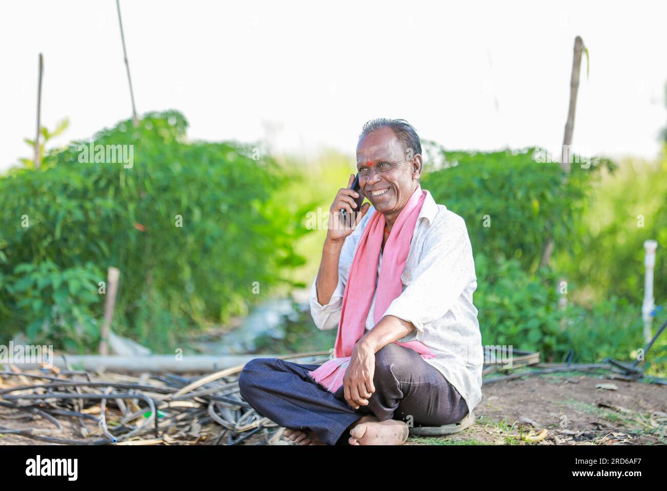heureux fermier assis dans le sol parlant au téléphone, vieux fermier indien Banque D'Images