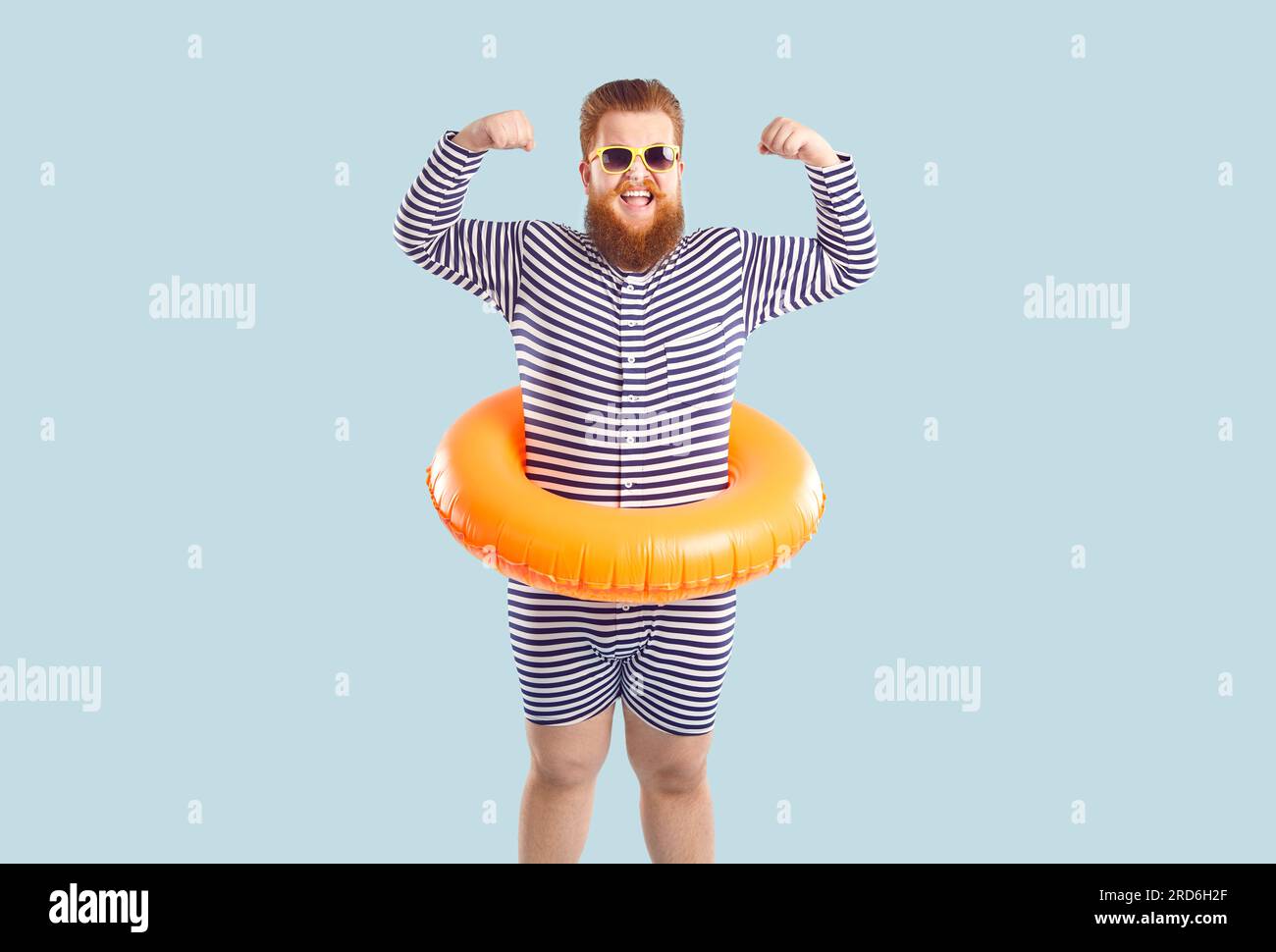 Homme gras barbu drôle avec cercle gonflable pour la natation à la taille montre ses biceps. Banque D'Images