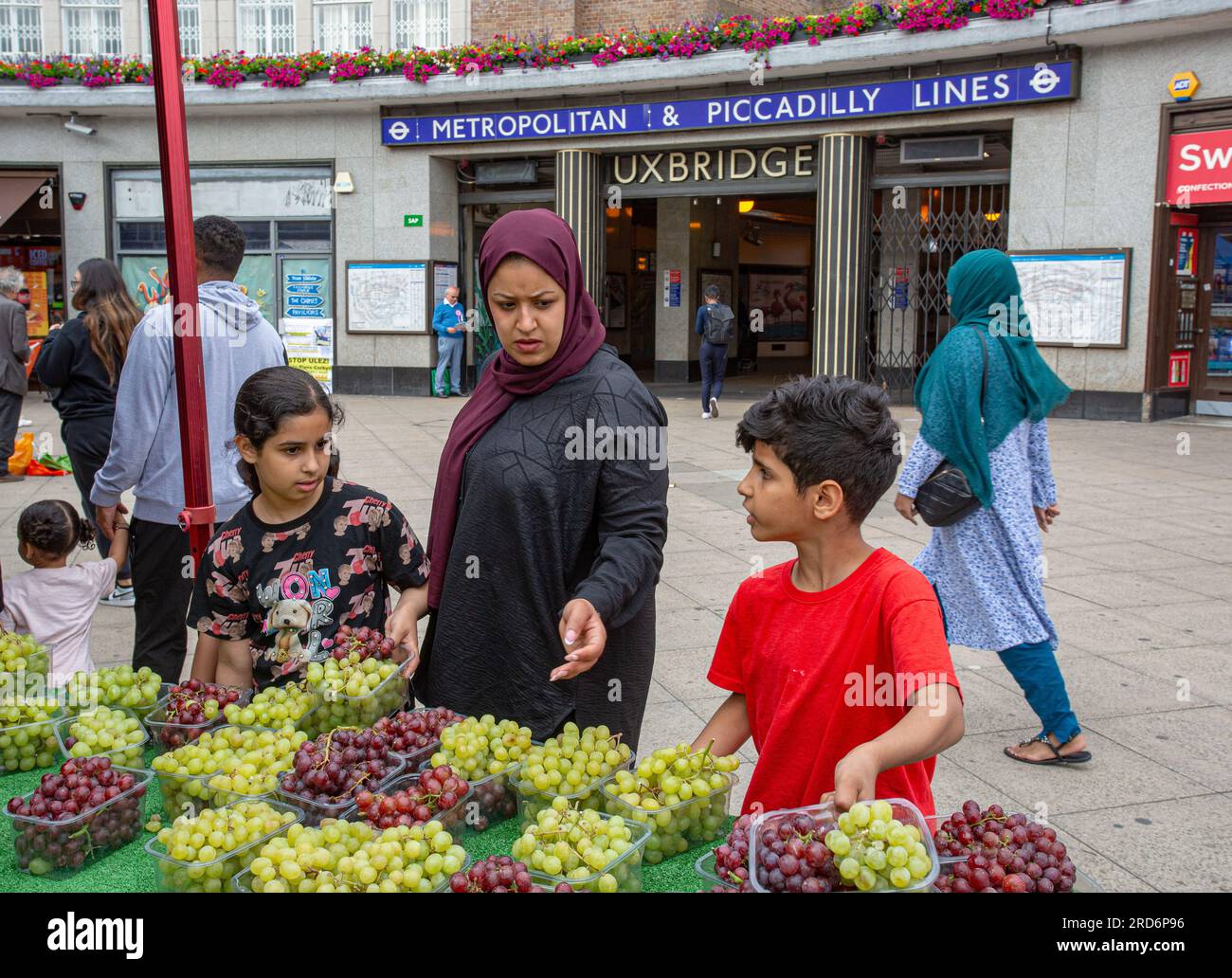 Uxbridge, Royaume-Uni. 18 juillet 2023. Deux jours avant l'élection partielle politique, la famille achète des fruits et légumes devant la station de métro Uxbridge, le 18 juillet 2023, à Londres, en Angleterre. La circonscription d'Uxbridge et de South Ruislip est l'une des trois élections partielles locales tenues le même jour, mais Uxbridge a été représentée au Parlement par l'ancien Premier ministre conservateur Boris Johnson pendant huit ans avant de démissionner de son poste de député. Il sera contesté par 17 candidats le 20 juillet. Crédit : horst friedrichs/Alamy Live News Banque D'Images