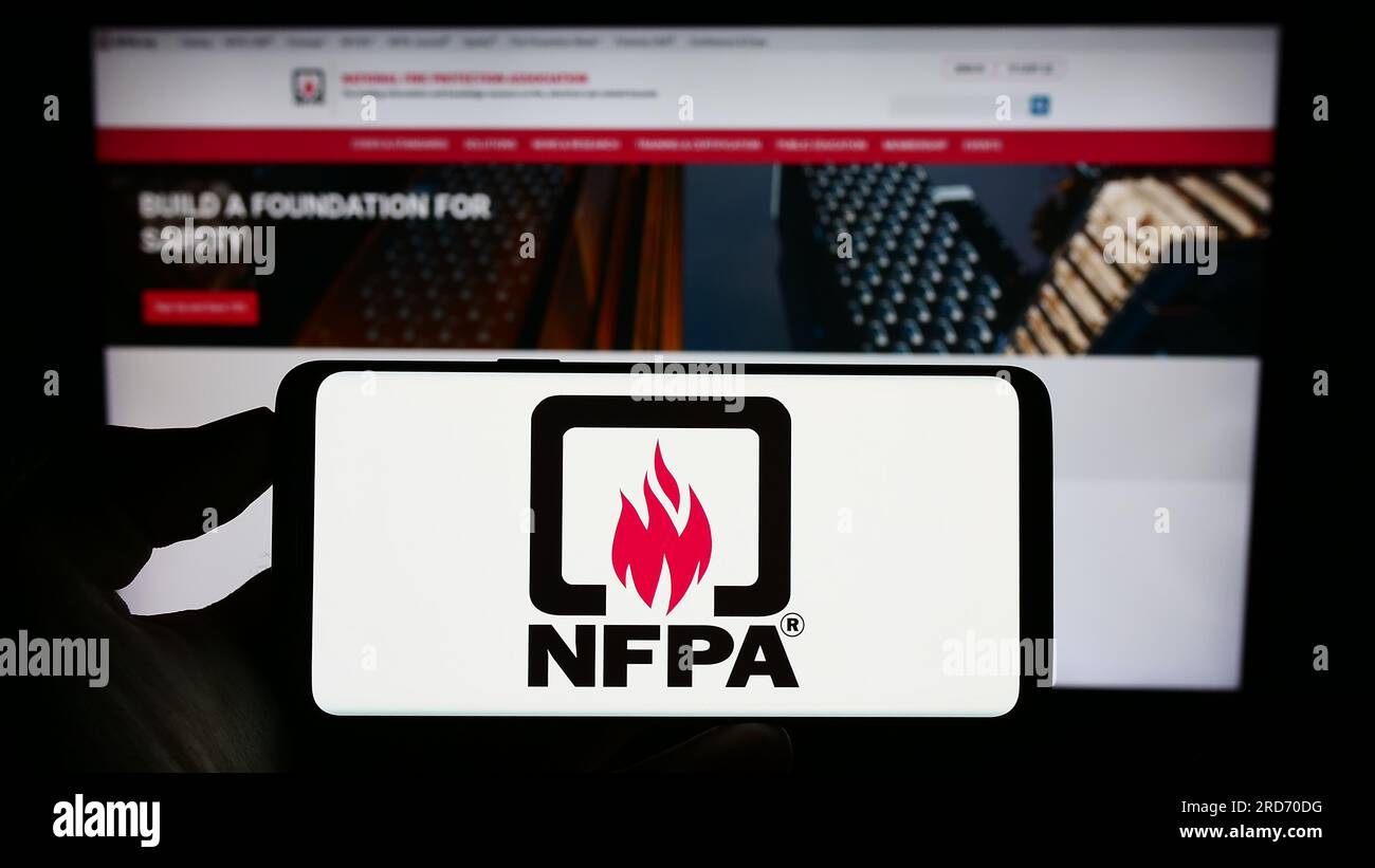 Personne tenant un téléphone portable avec le logo de la National Fire protection Association (NFPA) sur l'écran devant la page Web. Concentrez-vous sur l'affichage du téléphone. Banque D'Images