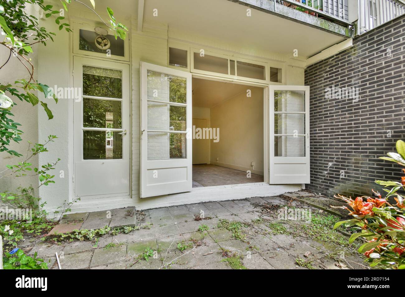 l'extérieur d'une maison avec une porte ouverte et quelques plantes poussant dans la cour avant, par une journée ensoleillée Banque D'Images