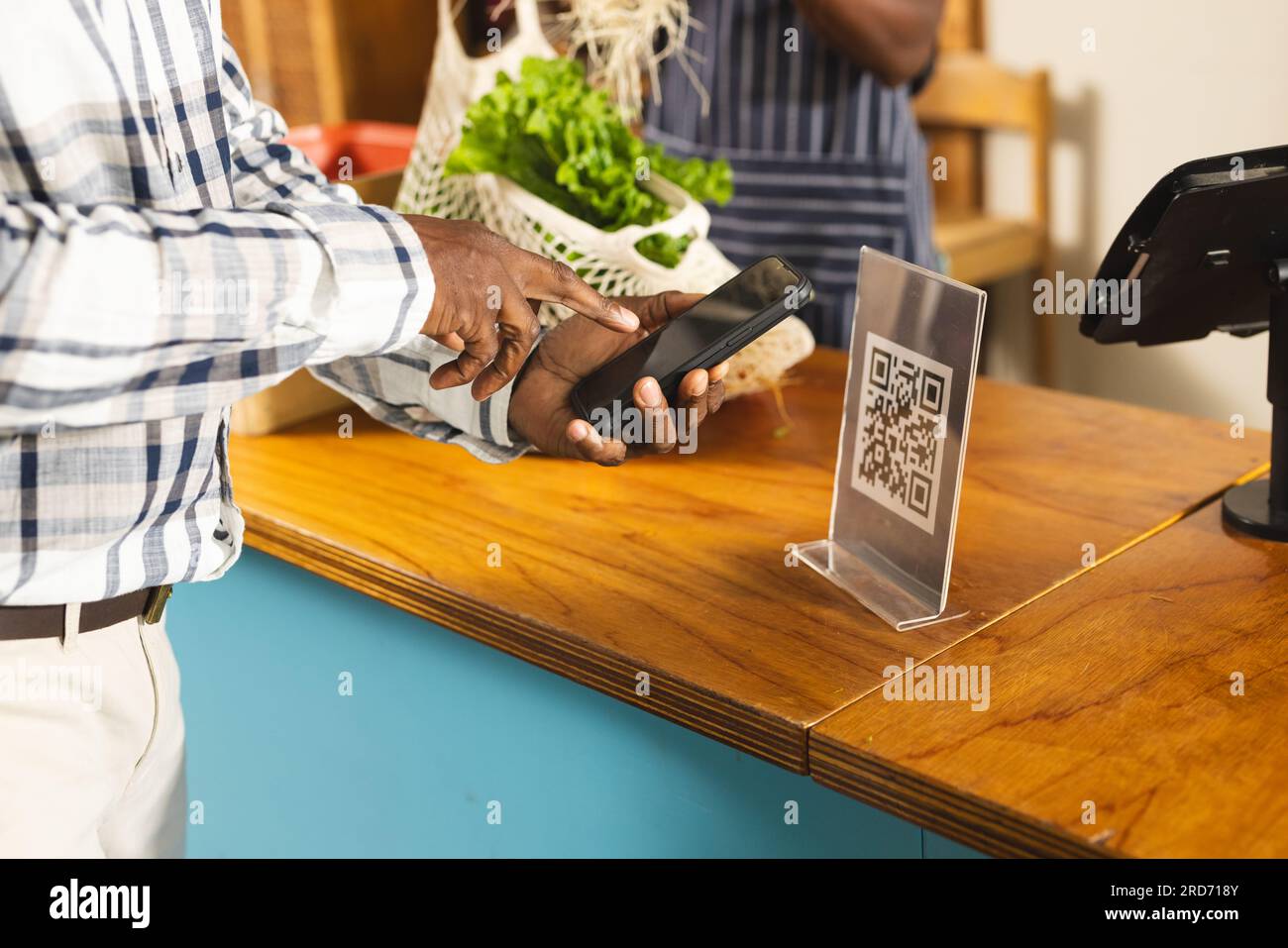 Homme afro-américain senior payant avec smartphone en utilisant le code qr à l'épicerie biologique d'aliments naturels Banque D'Images