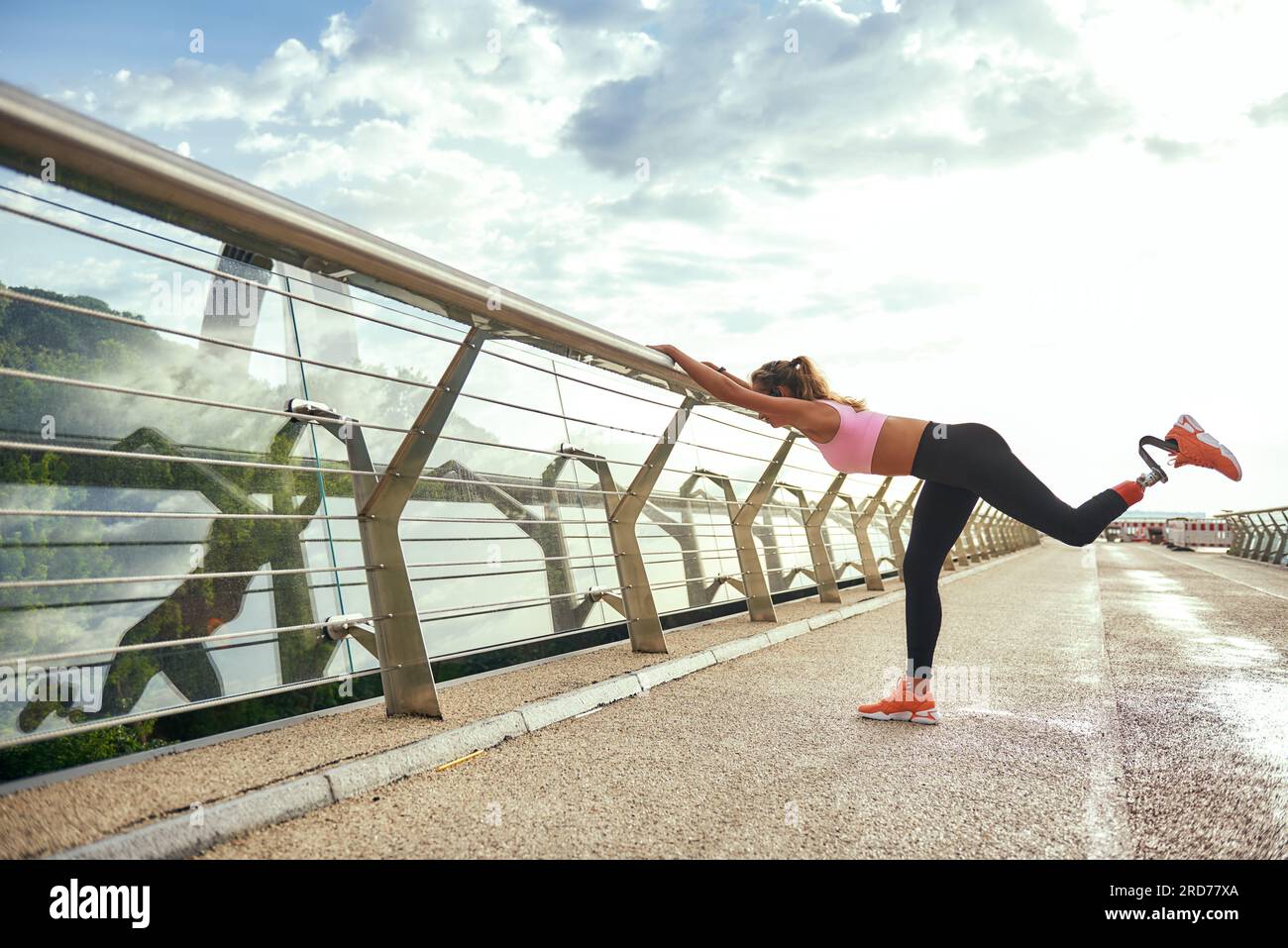Entraînement matinal. Femme athlétique handicapée avec jambe prothétique en vêtements de sport faisant des exercices de sport tout en se tenant debout sur le pont. Vue latérale Banque D'Images