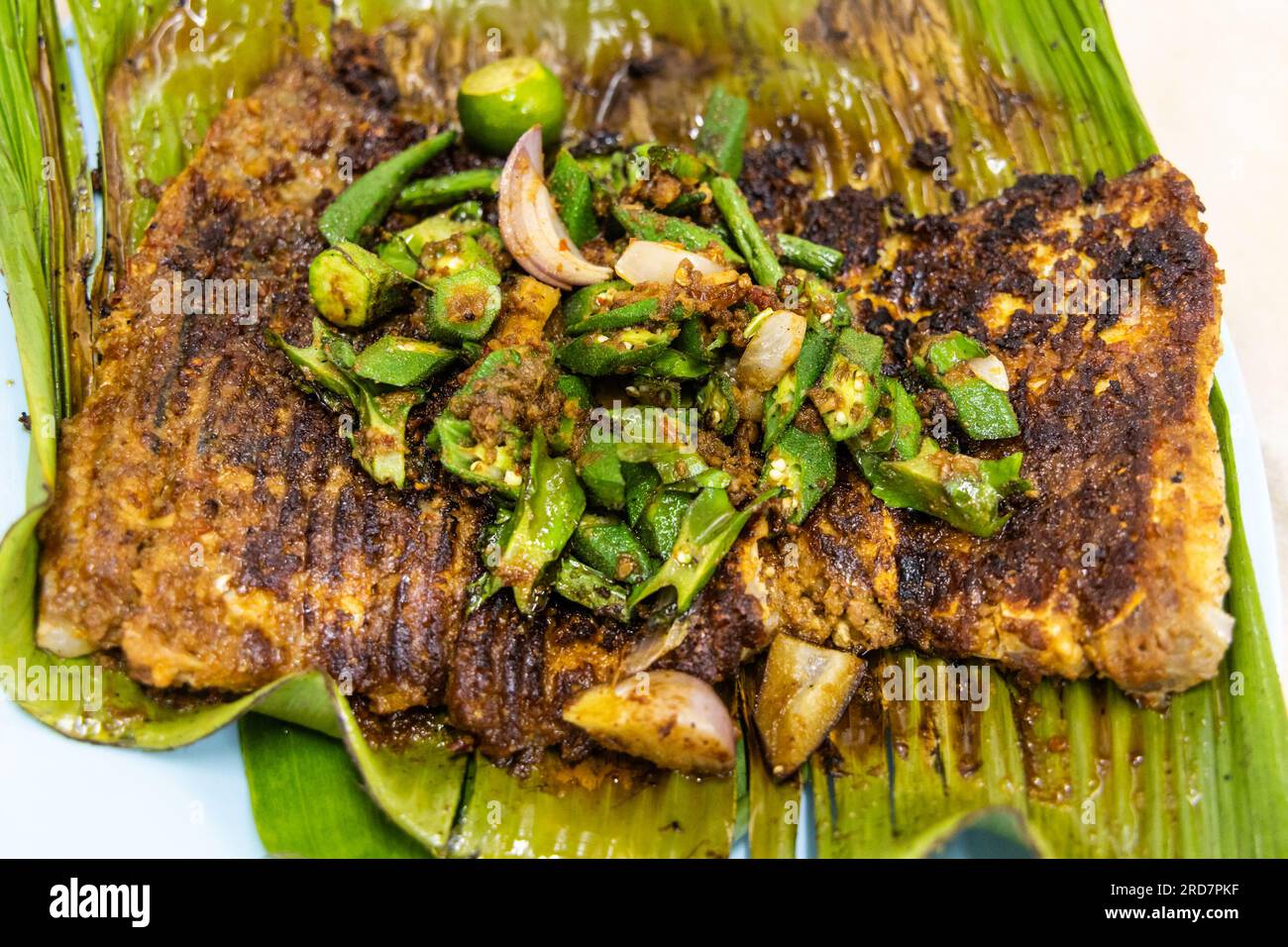 Gros plan vue aérienne de poisson raide grillé avec des épices garnies de légumes d'okra sur la feuille de bananier nourriture populaire en Malaisie Banque D'Images