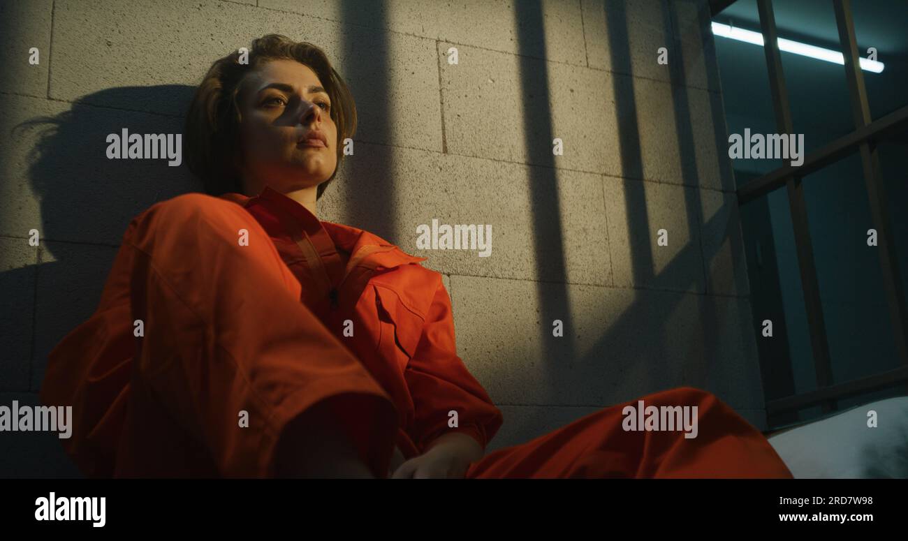 Prisonnière en uniforme orange assise sur le lit dans la cellule de prison, lit la Bible. Une femme criminelle purge une peine d'emprisonnement pour crime en prison ou dans un établissement correctionnel. Banque D'Images