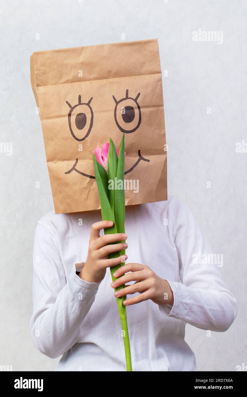 Un sac cadeau en carton avec un sourire peint a été mis sur la tête de l'enfant. Le concept de cadeau anonyme. Banque D'Images