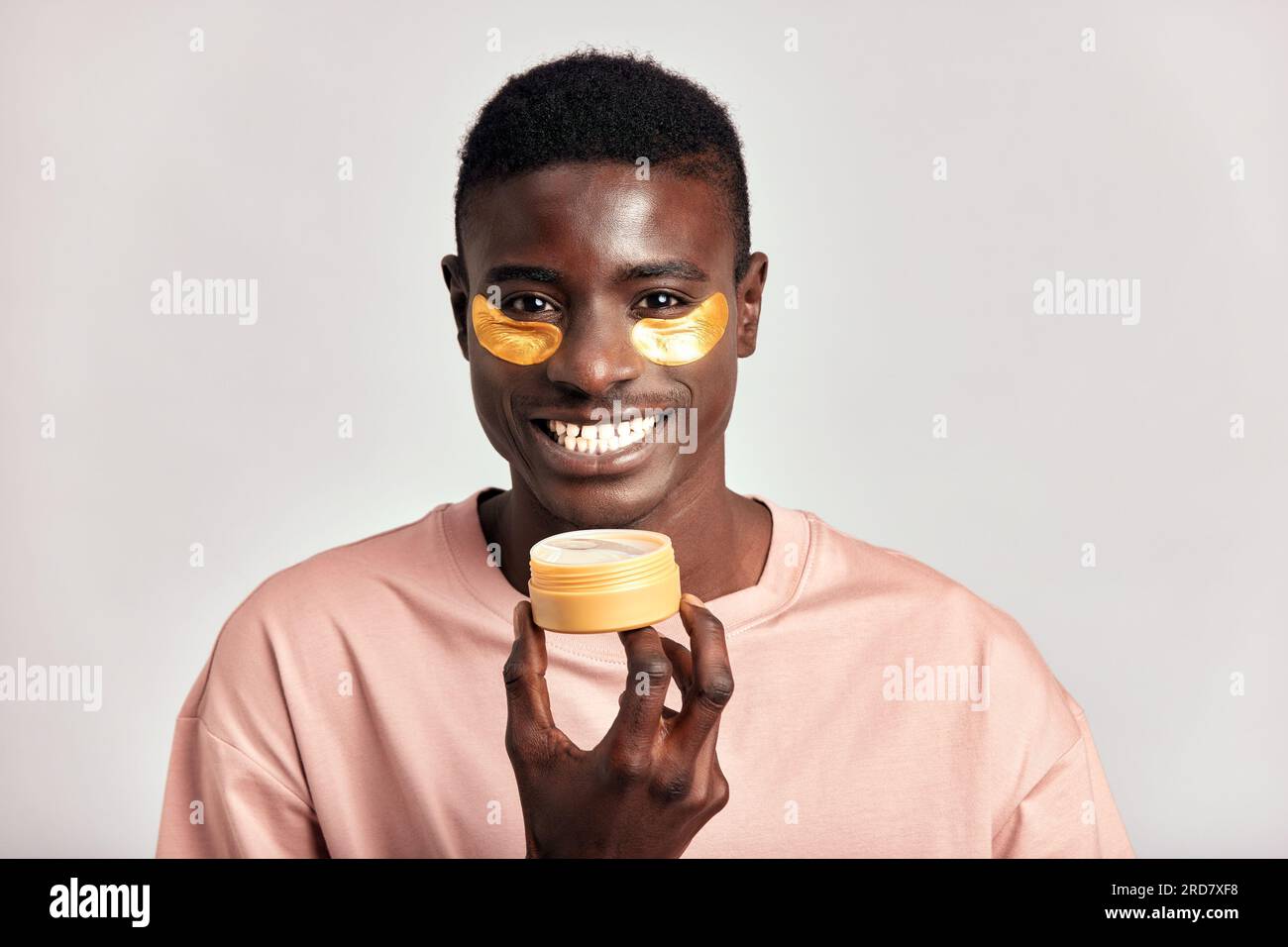 Jeune beau gars noir appliquant des patchs cosmétiques hydrogel sous ses yeux à partir d'un étui dans sa main. L'homme millénaire afro-américain pratique la voiture de peau Banque D'Images