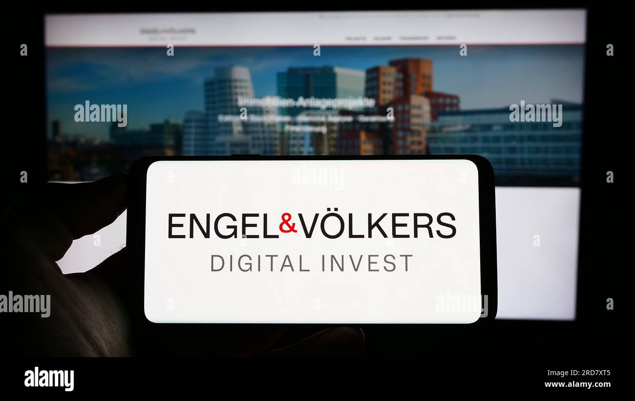 Personne tenant le téléphone portable avec le logo de la société immobilière allemande EV Digital Invest AG sur l'écran en face de la page Web. Concentrez-vous sur l'affichage du téléphone. Banque D'Images