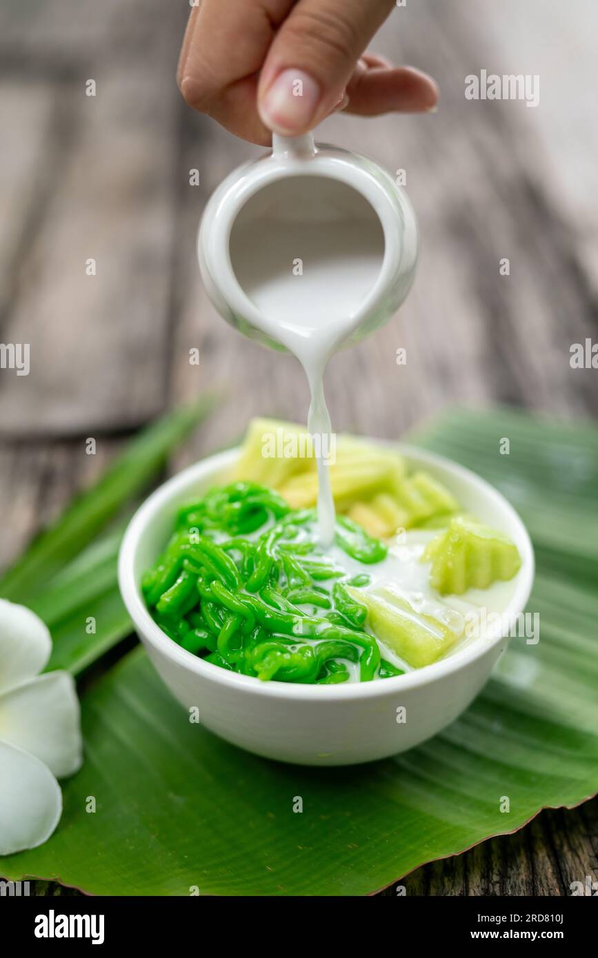 Gros plan de Lod Chong appétissant étant versé avec du lait de coco frais sur feuille de banane sur fond de bois. Banque D'Images