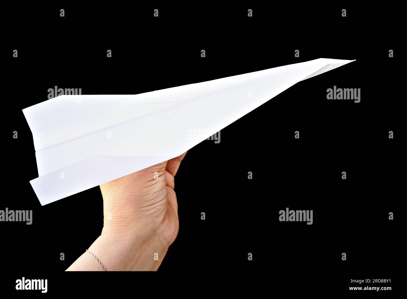Main de femme tenant l'avion de papier sur fond noir Banque D'Images