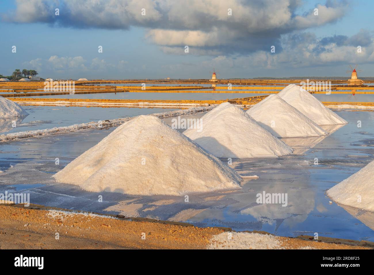 Piles de sels parmi les marais salants avec des moulins à vent en arrière-plan au coucher du soleil, Saline Ettore e Infersa, Marsala, province de Trapani Banque D'Images