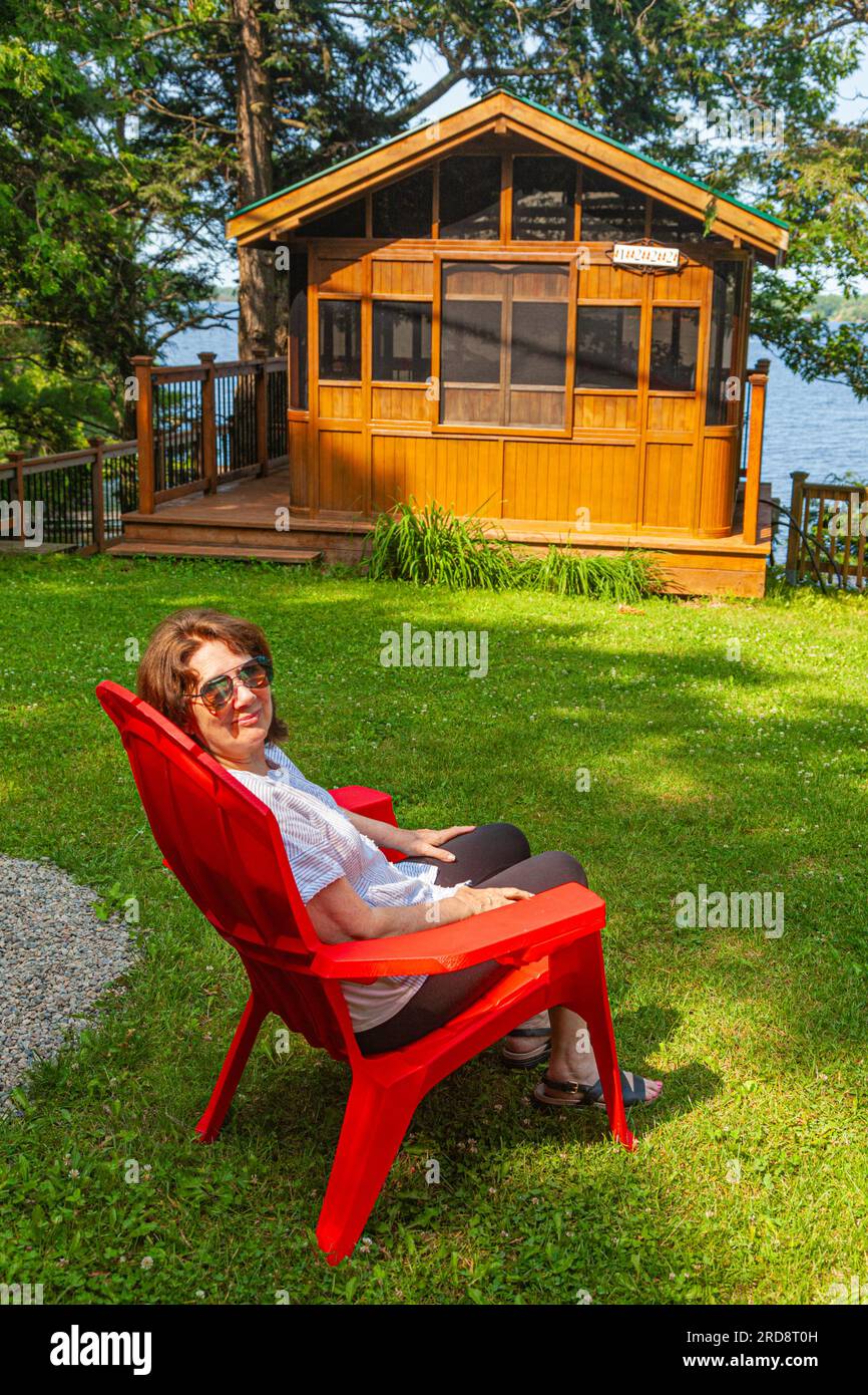Jeune grand-mère se détendant dans une chaise rouge près du lac Sparrow à Muskoka Ontario Canada Banque D'Images
