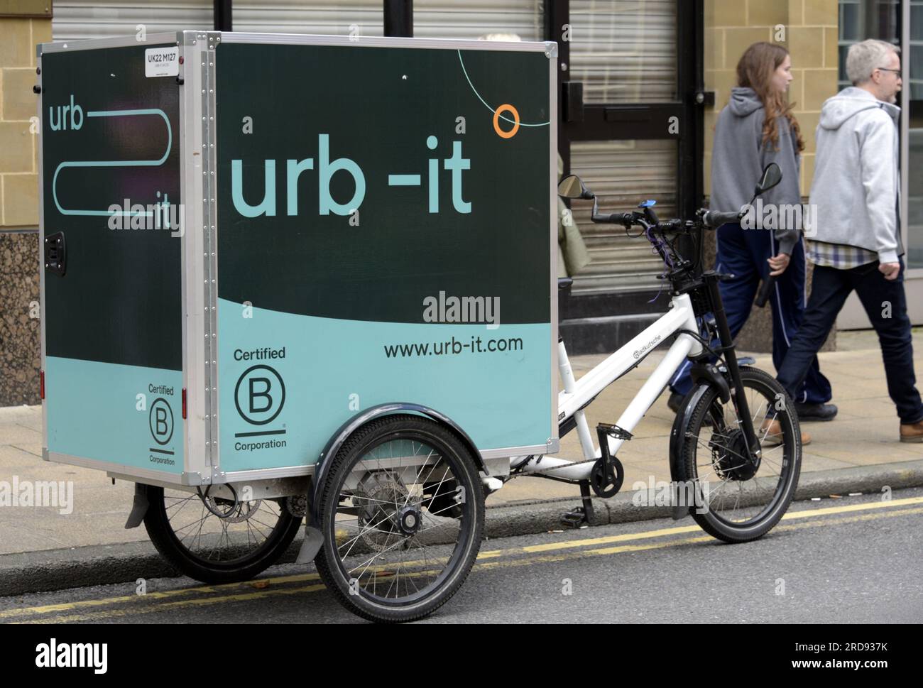 Urb - IT tricycle avec conteneur de colis, services de livraison de colis e-commerce dans les grandes villes, garé au centre de Manchester, Royaume-Uni, en juillet 2023, peole marcher devant Banque D'Images