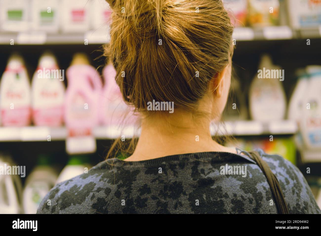 Vue arrière d'une jeune femme adulte méconnaissable avec les cheveux vers le haut regardant l'étagère en choisissant quel détergent à lessive acheter au supermarché à l'intérieur. Banque D'Images