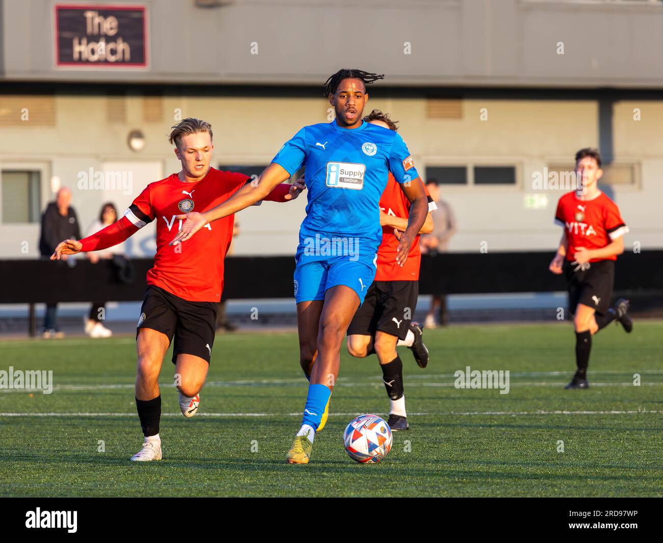 Edy Maieco, joueur des Warrington Rylands, traverse un milieu de terrain poursuivi par un défenseur de Stockport Town au Stockport Sports Village sur un terrain 3G. Banque D'Images