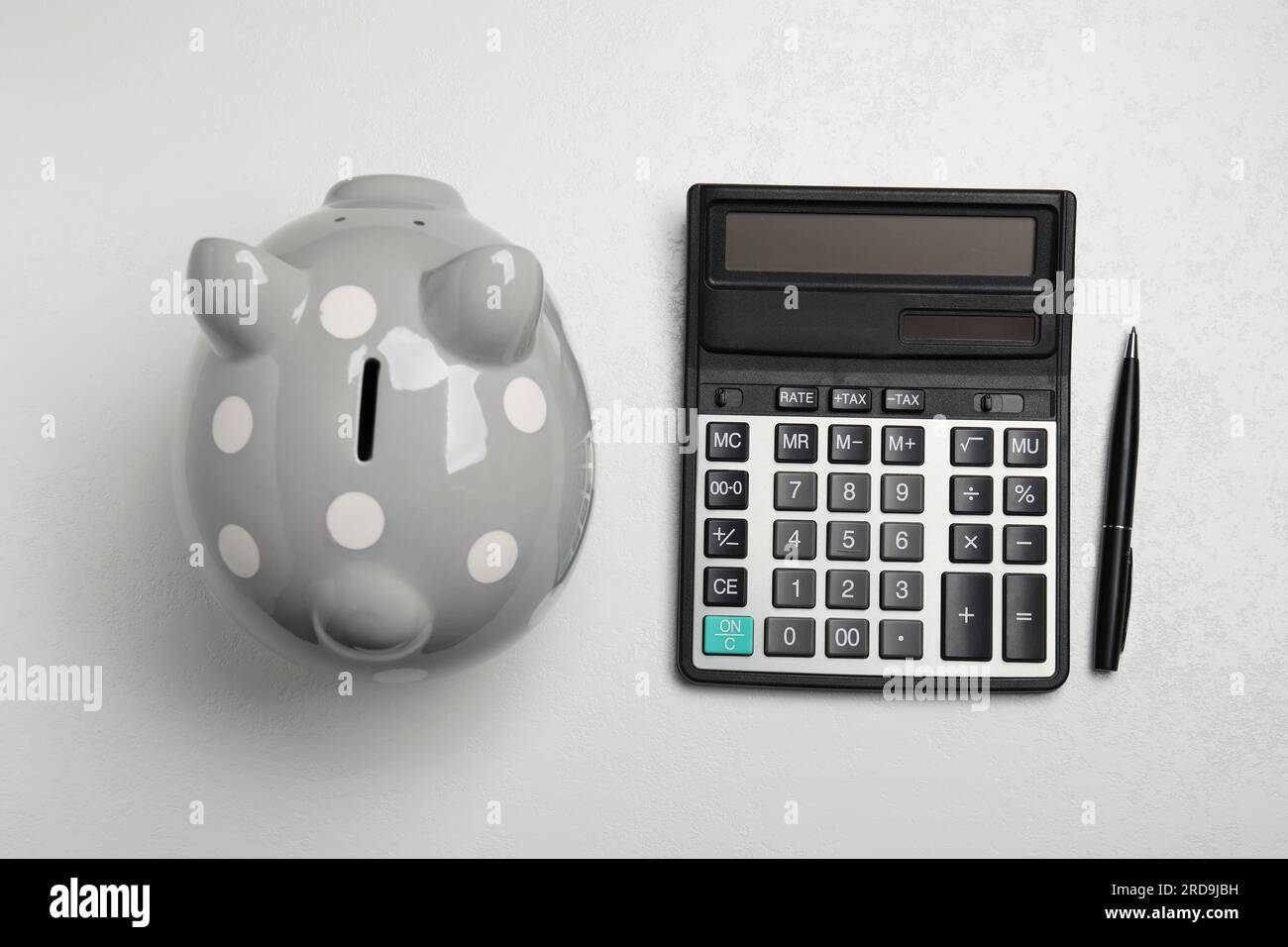 Calculatrice, stylo et tirelire sur table blanche, pose à plat Banque D'Images