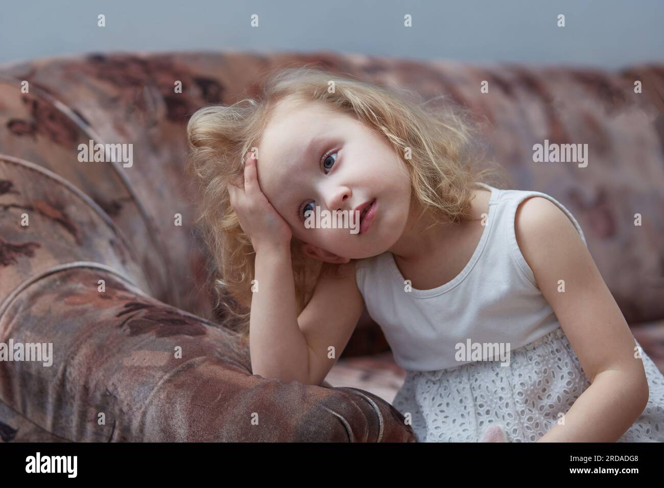 Un enfant triste s'ennuie. Fille aux cheveux bouclés est triste assise sur le canapé à la maison Banque D'Images