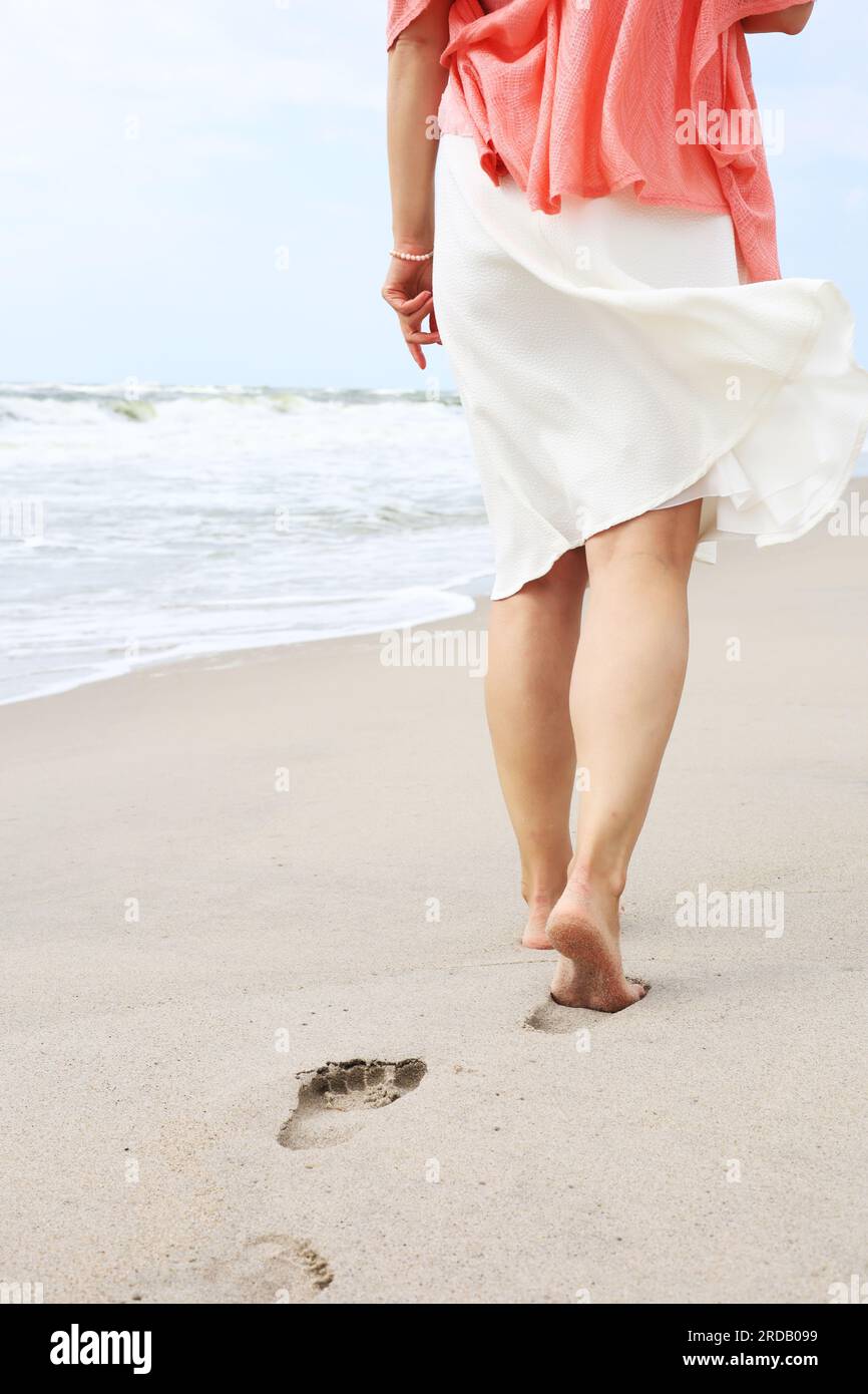 Excursion à la plage - une femme marche le long d'une plage de sable de manière détendue, laissant des empreintes de pas dans le sable. Gros plan des pieds et tibias des femmes sur sable doré Banque D'Images Excursion à la plage - une femme marche le long d'une plage de sable de manière détendue, laissant des empreintes de pas dans le sable. Gros plan des pieds et tibias des femmes sur sable doré Banque D'Images