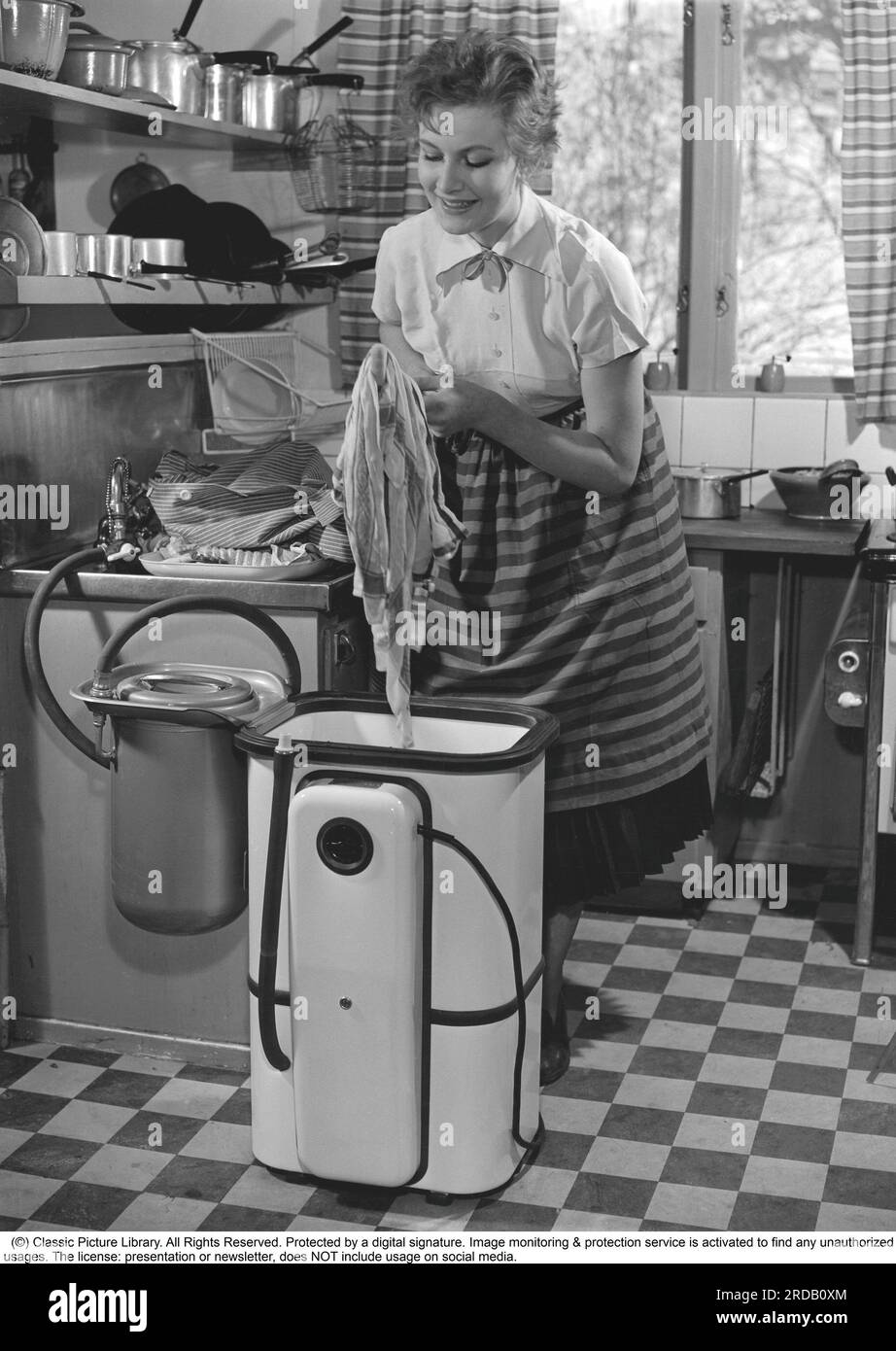 Faire le linge dans le 1950s. Une dame utilise un lave-linge dans la cuisine. Une cuisine typique de 1950s avec un évier et des casseroles et des poêles sur les étagères ci-dessus. Suède 1953 réf. 2317 Banque D'Images