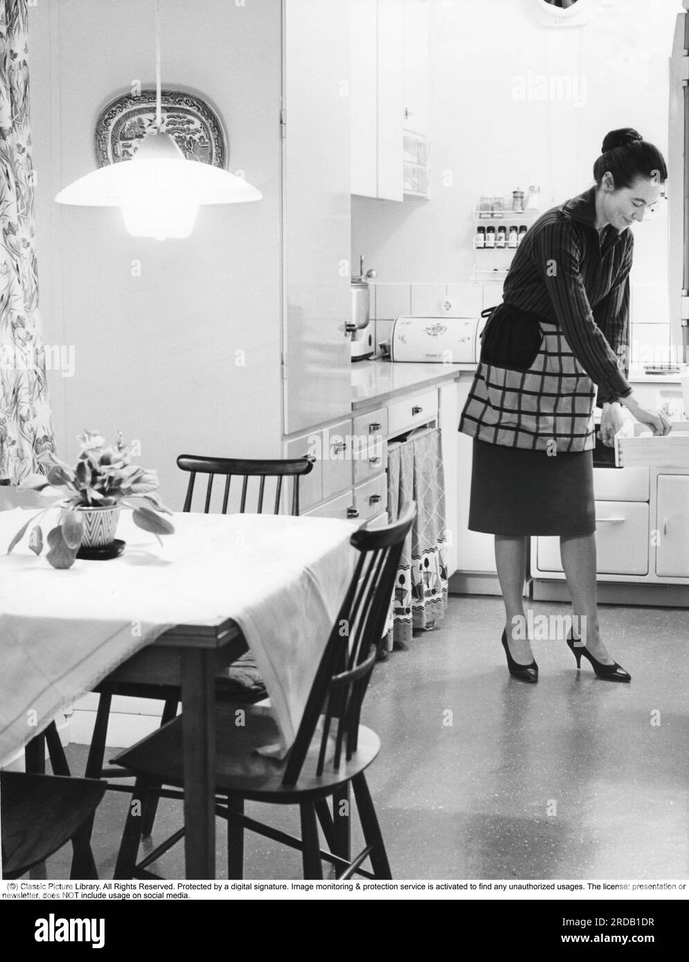 Dans la cuisine 1960s. Intérieur d'une cuisine et une femme prenant quelque chose d'un tiroir de cuisine. Suède 1960 Banque D'Images
