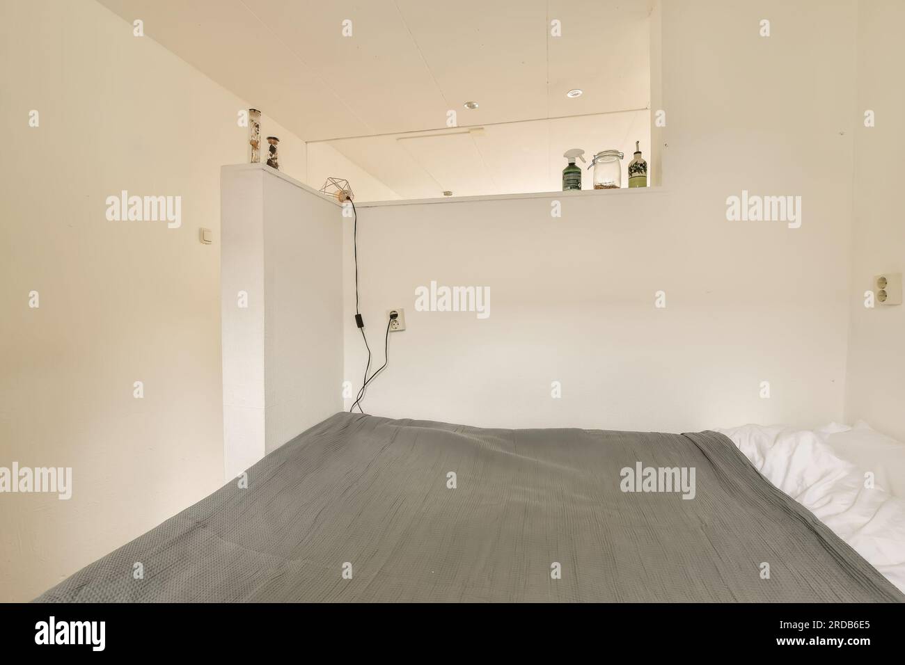 un lit dans le coin d'une chambre qui est blanc et a des draps gris sur son bord inférieur Banque D'Images