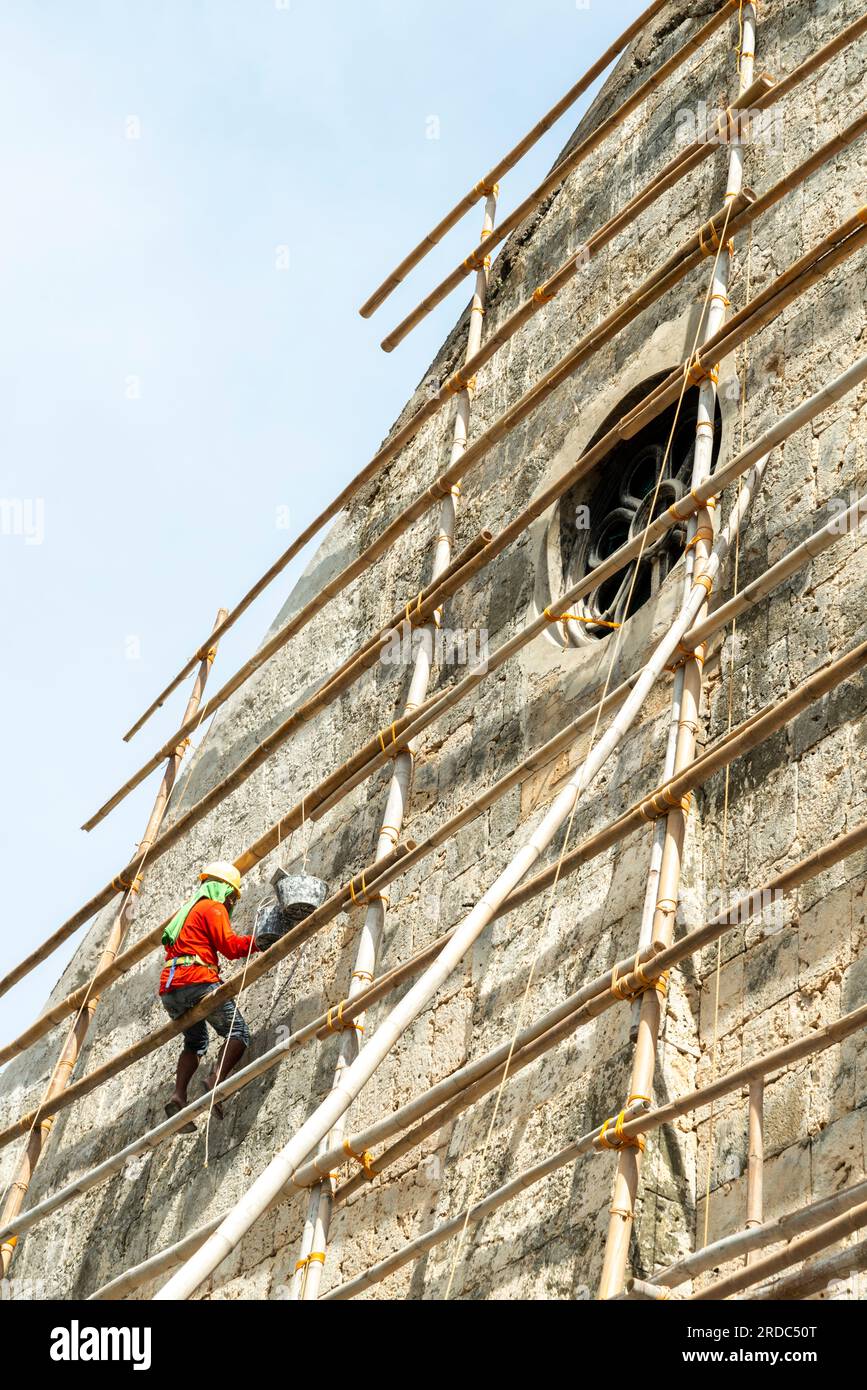 Île de Cebu, Philippines-27 janvier 2023 : utilisant des poteaux de bambou comme échafaudage et portant des tongs sur ses pieds, l'ouvrier applique de la peinture blanche t Banque D'Images