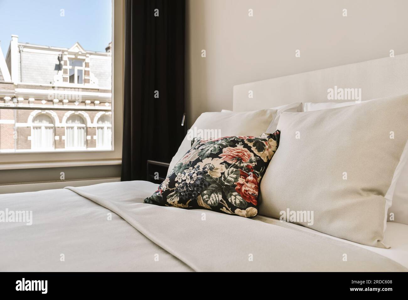 un lit avec des draps blancs et des oreillers devant une grande fenêtre donnant sur la cityscapea Banque D'Images
