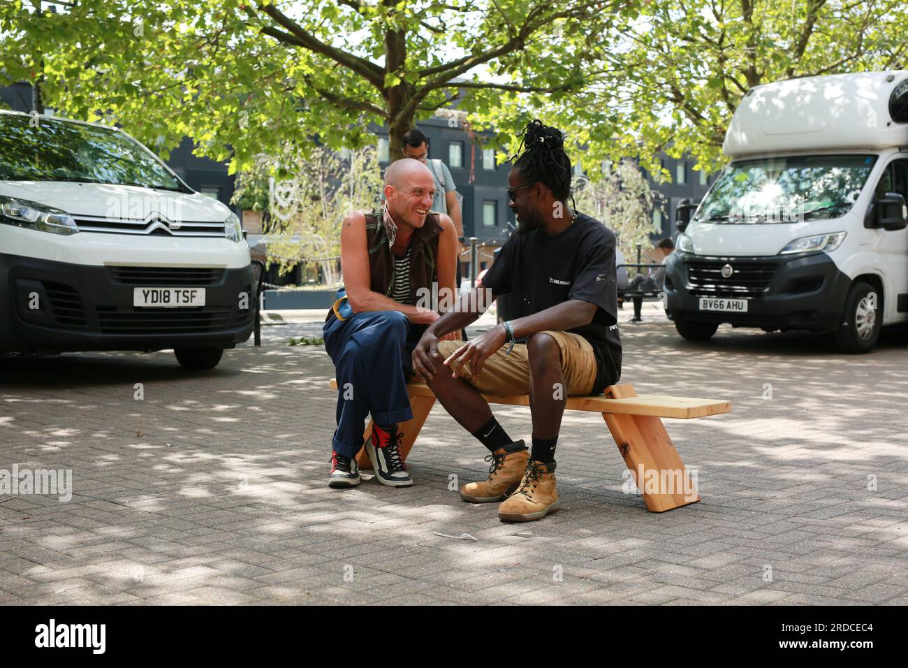 Londres, Royaume-Uni. 20 juillet 2023. 'Bench invasion' de la Compagnie Krak. Dans la performance 'Bench invasion', l'artiste belge Dieter Peter Raphaël Missiaen se déplace dans l'espace public avec dix personnes locales, chacune avec un banc sous le bras, à la recherche de contacts. À un moment inopiné, ils installent des bancs et invitent activement les gens à s’asseoir devant eux. De cette façon, il (re)connecte les gens. Le Festival d'ensemble est un festival de quatre jours de théâtre, de cirque, de danse, de musique et d'art numérique gratuits au Royal Victoria Dock. Ensemble Festival explore les thèmes de l'écologie, de la vie moderne et de la reconnexion, et comprend deux jours de pop-up per Banque D'Images