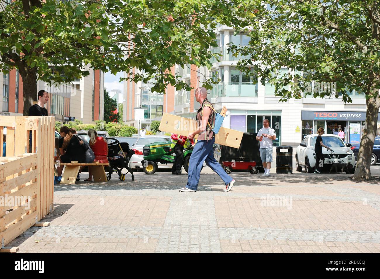 Londres, Royaume-Uni. 20 juillet 2023. 'Bench invasion' de la Compagnie Krak. Dans la performance 'Bench invasion', l'artiste belge Dieter Peter Raphaël Missiaen se déplace dans l'espace public avec dix personnes locales, chacune avec un banc sous le bras, à la recherche de contacts. À un moment inopiné, ils installent des bancs et invitent activement les gens à s’asseoir devant eux. De cette façon, il (re)connecte les gens. Le Festival d'ensemble est un festival de quatre jours de théâtre, de cirque, de danse, de musique et d'art numérique gratuits au Royal Victoria Dock. Ensemble Festival explore les thèmes de l'écologie, de la vie moderne et de la reconnexion, et comprend deux jours de pop-up per Banque D'Images