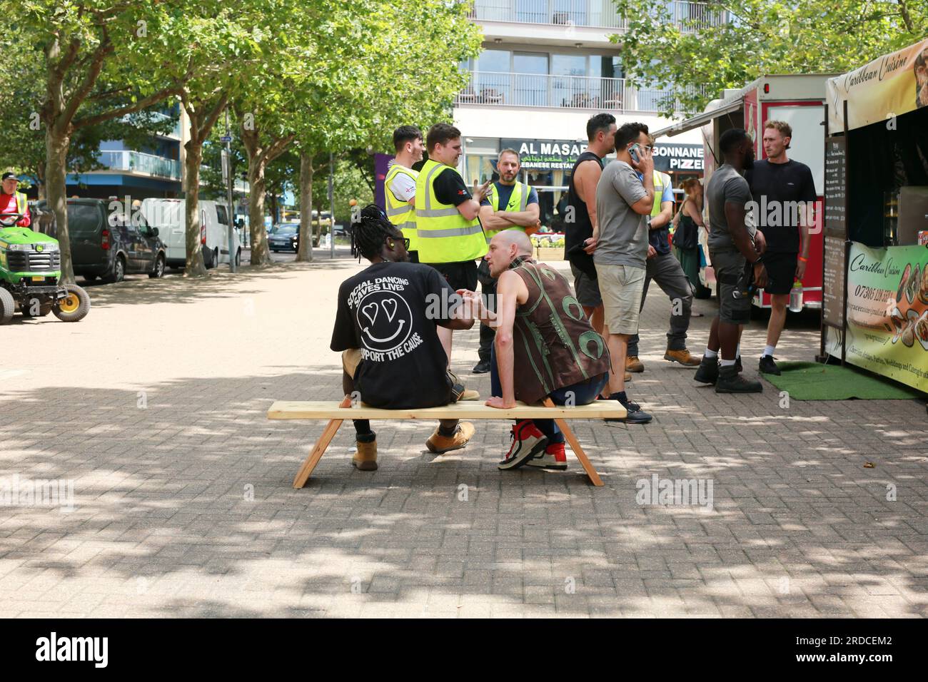 Londres, Royaume-Uni. 20 juillet 2023. 'Bench invasion' de la Compagnie Krak. Dans la performance 'Bench invasion', l'artiste belge Dieter Peter Raphaël Missiaen se déplace dans l'espace public avec dix personnes locales, chacune avec un banc sous le bras, à la recherche de contacts. À un moment inopiné, ils installent des bancs et invitent activement les gens à s’asseoir devant eux. De cette façon, il (re)connecte les gens. Le Festival d'ensemble est un festival de quatre jours de théâtre, de cirque, de danse, de musique et d'art numérique gratuits au Royal Victoria Dock. Ensemble Festival explore les thèmes de l'écologie, de la vie moderne et de la reconnexion, et comprend deux jours de pop-up per Banque D'Images