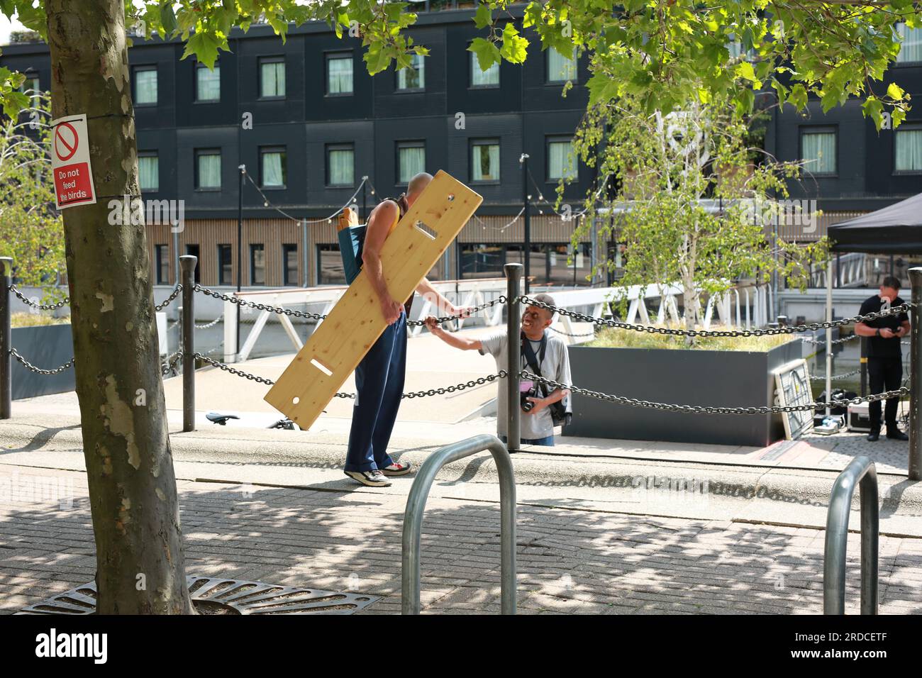 Londres, Royaume-Uni. 20 juillet 2023. 'Bench invasion' de la Compagnie Krak. Dans la performance 'Bench invasion', l'artiste belge Dieter Peter Raphaël Missiaen se déplace dans l'espace public avec dix personnes locales, chacune avec un banc sous le bras, à la recherche de contacts. À un moment inopiné, ils installent des bancs et invitent activement les gens à s’asseoir devant eux. De cette façon, il (re)connecte les gens. Le Festival d'ensemble est un festival de quatre jours de théâtre, de cirque, de danse, de musique et d'art numérique gratuits au Royal Victoria Dock. Ensemble Festival explore les thèmes de l'écologie, de la vie moderne et de la reconnexion, et comprend deux jours de pop-up per Banque D'Images